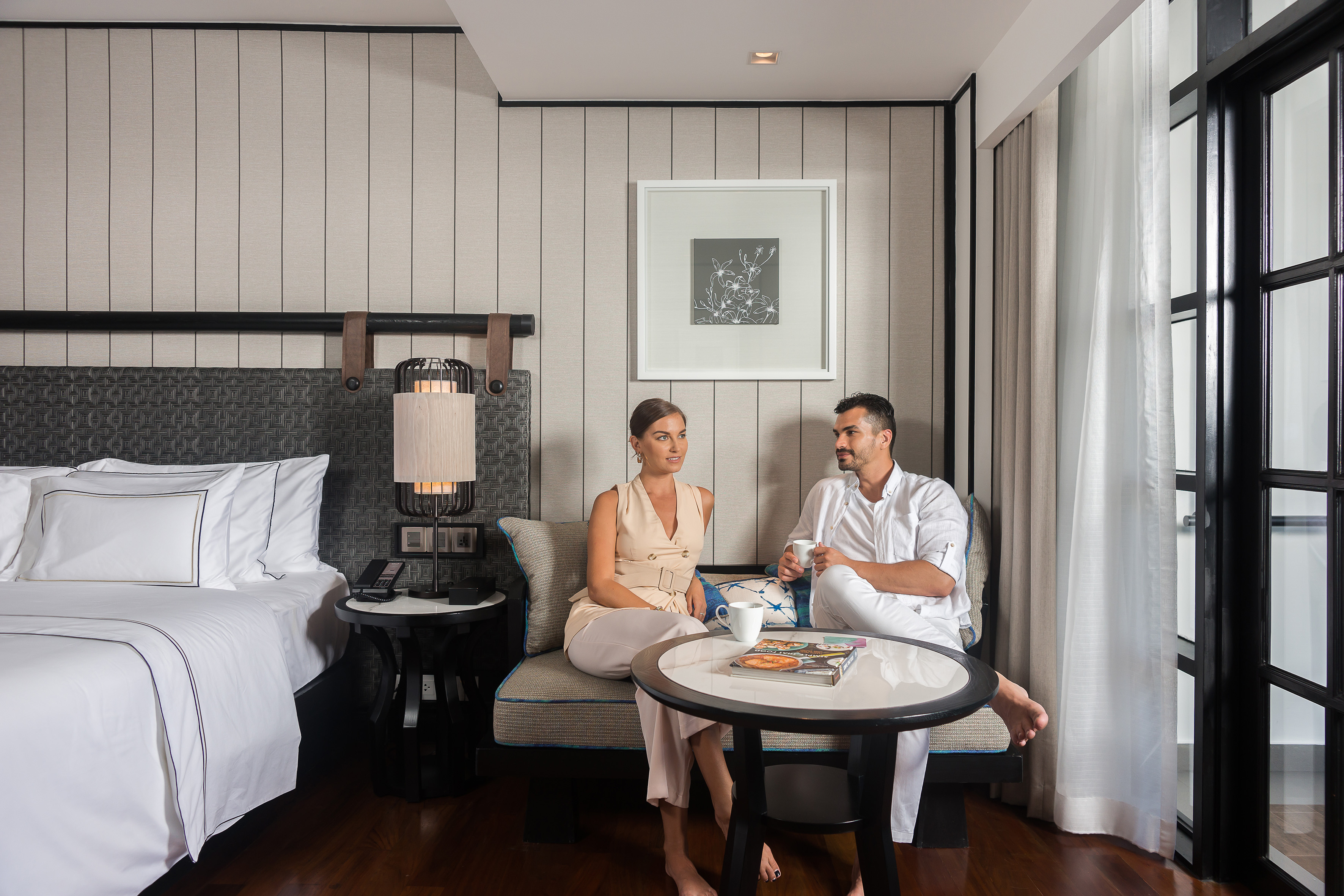 Couple relaxing in modern luxury hotel room with bed and sitting area.