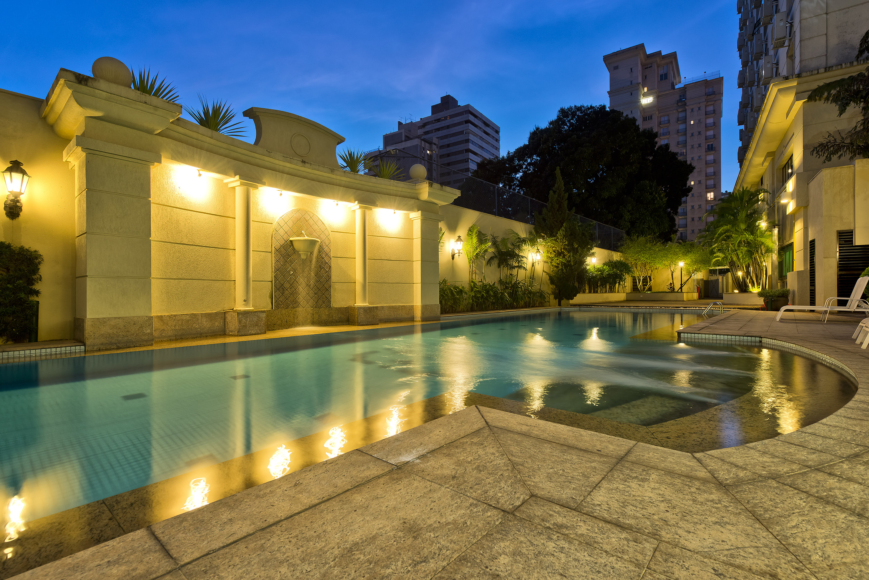 Luxury residential swimming pool at dusk, illuminated with warm lights.