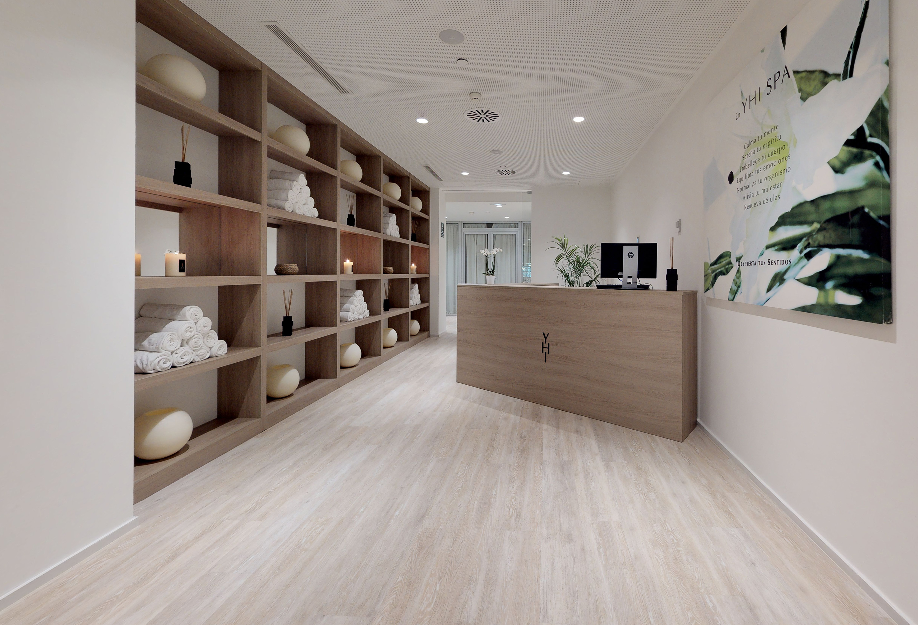 YHI Spa reception area with wooden desk, shelving, rolled white towels, and candles.