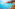 Boats on clear turquoise Mediterranean bay, rocky coast, green trees.