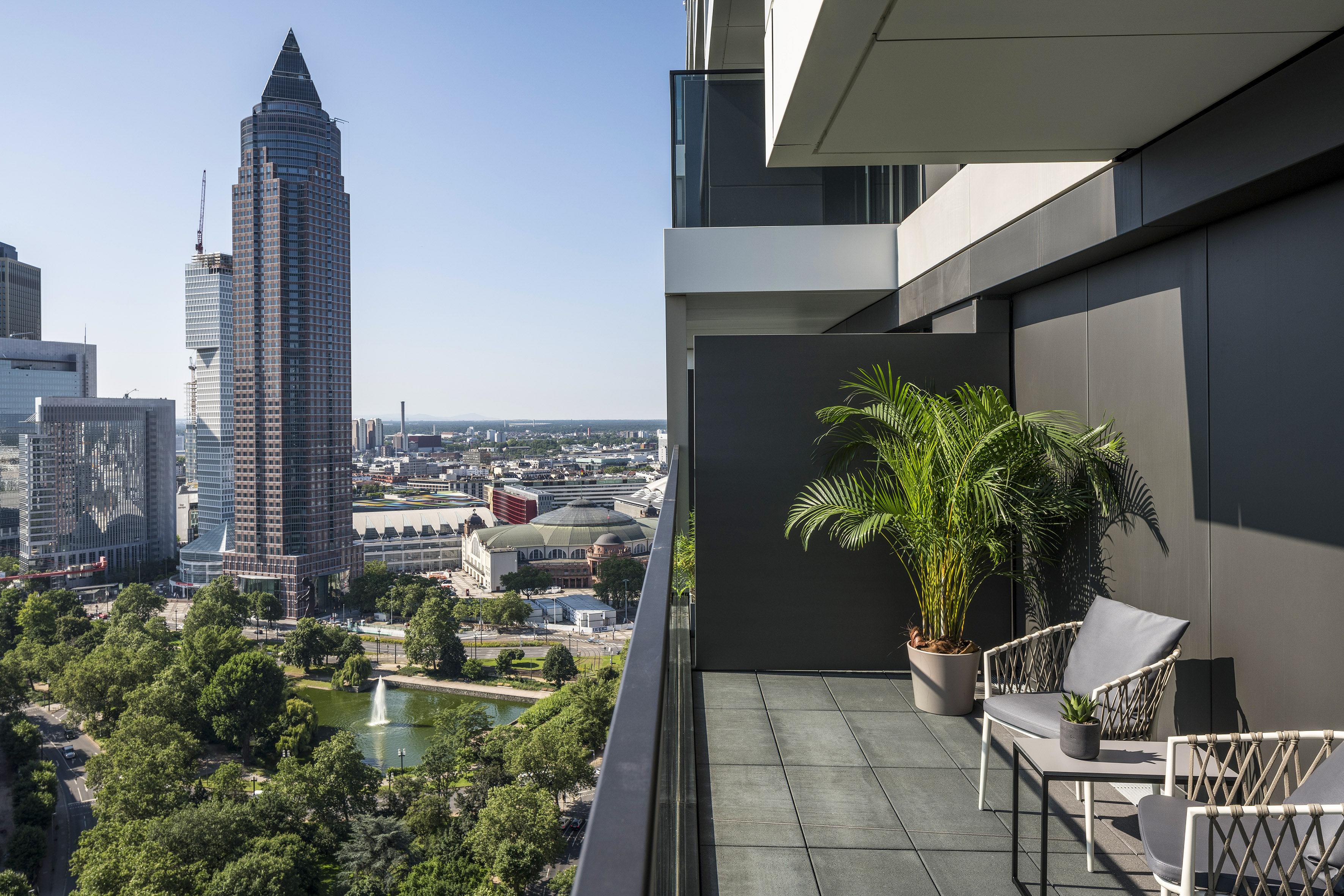 Modern balcony overlooking Frankfurt skyline with Messeturm and park.