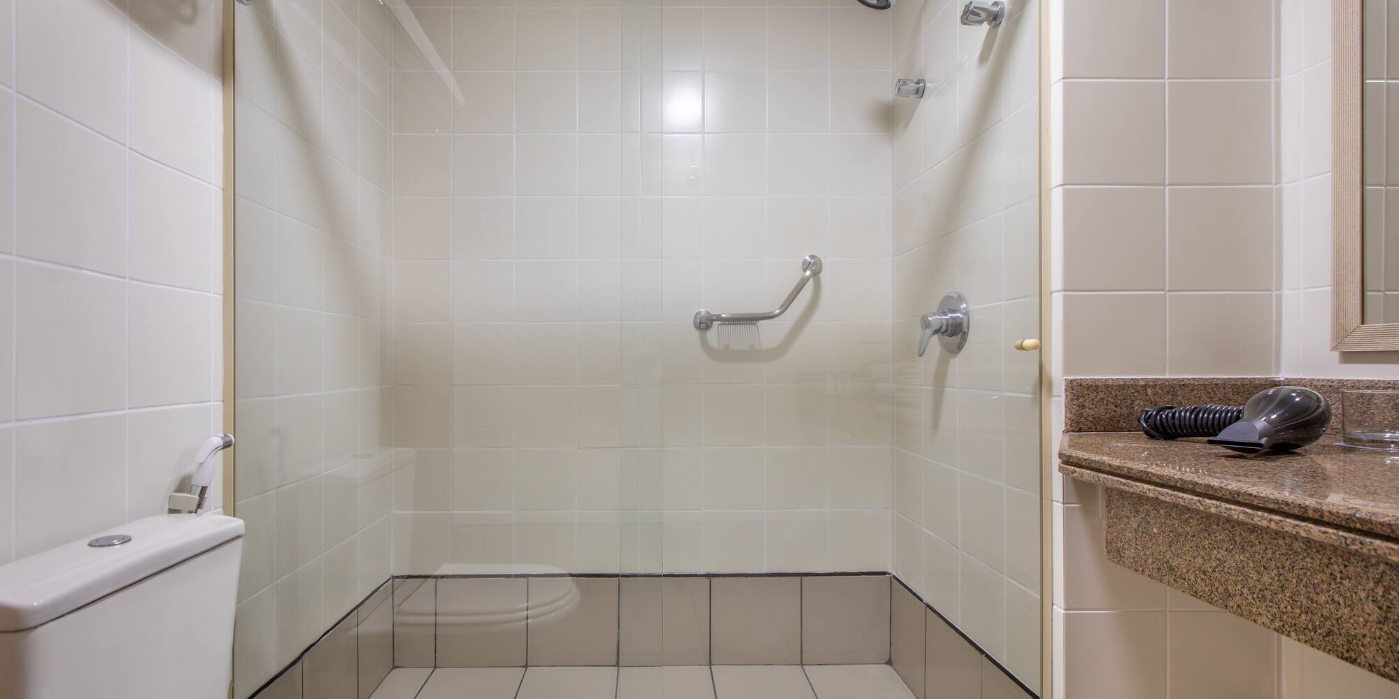 Hotel bathroom with accessible tiled shower, grab bar, toilet, and vanity.