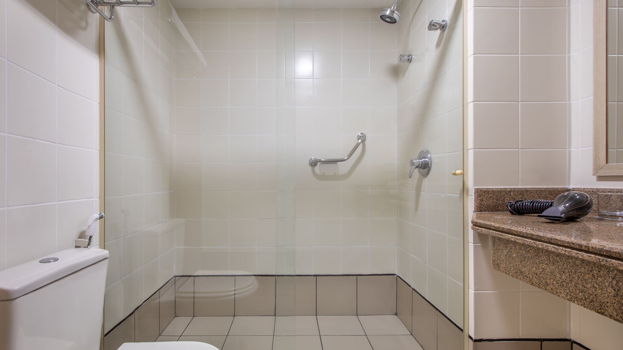 Hotel bathroom with accessible tiled shower, grab bar, toilet, and vanity.