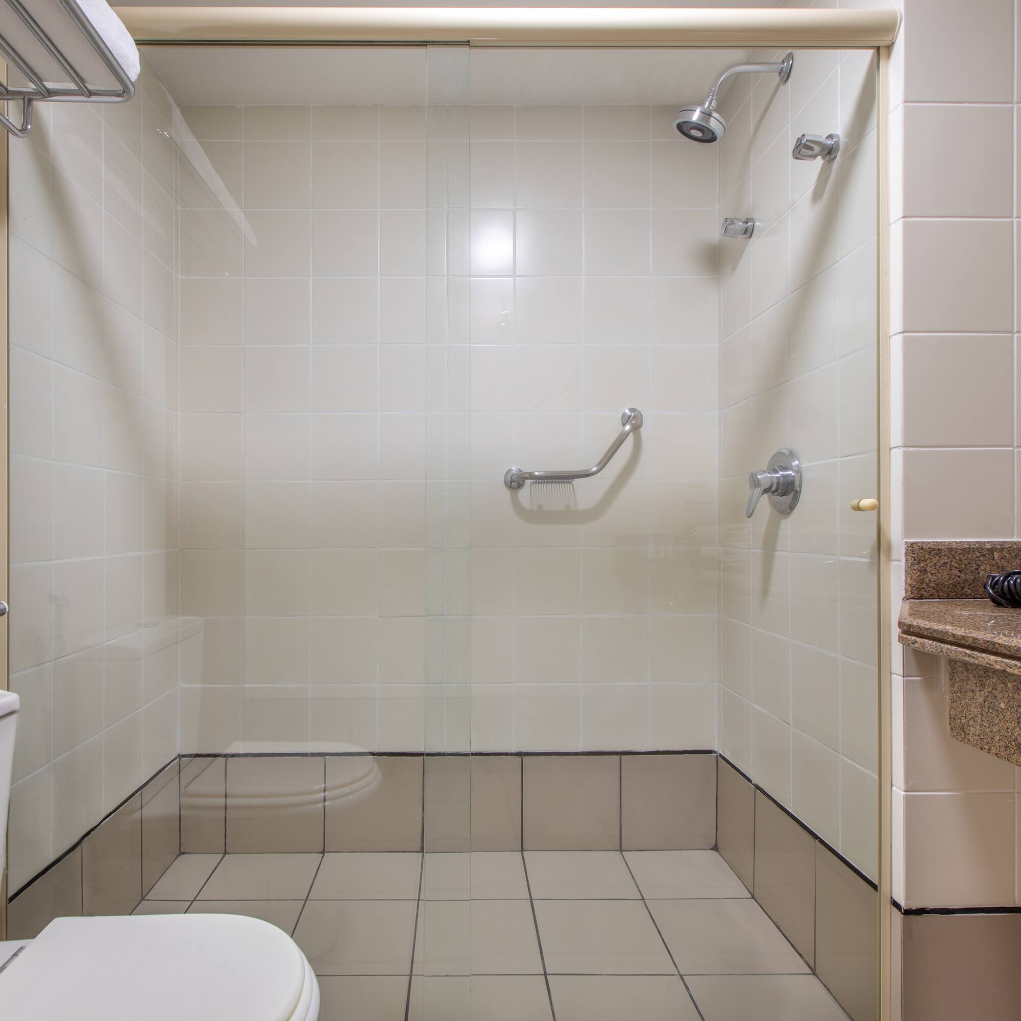 Hotel bathroom with accessible tiled shower, grab bar, toilet, and vanity.