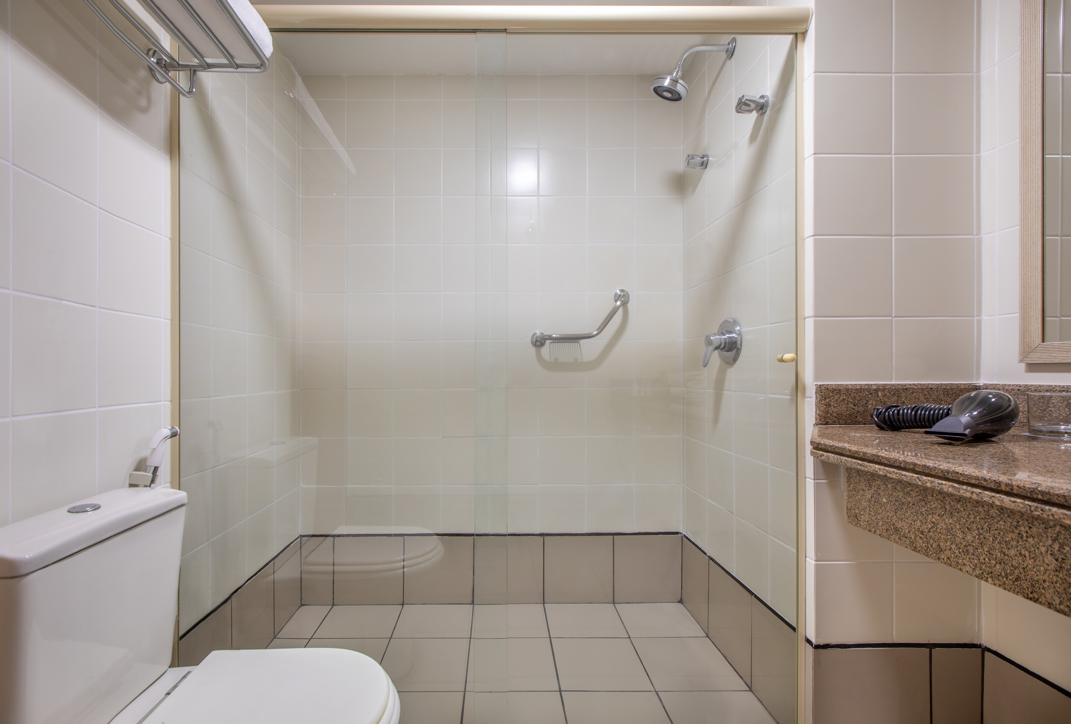 Hotel bathroom with accessible tiled shower, grab bar, toilet, and vanity.