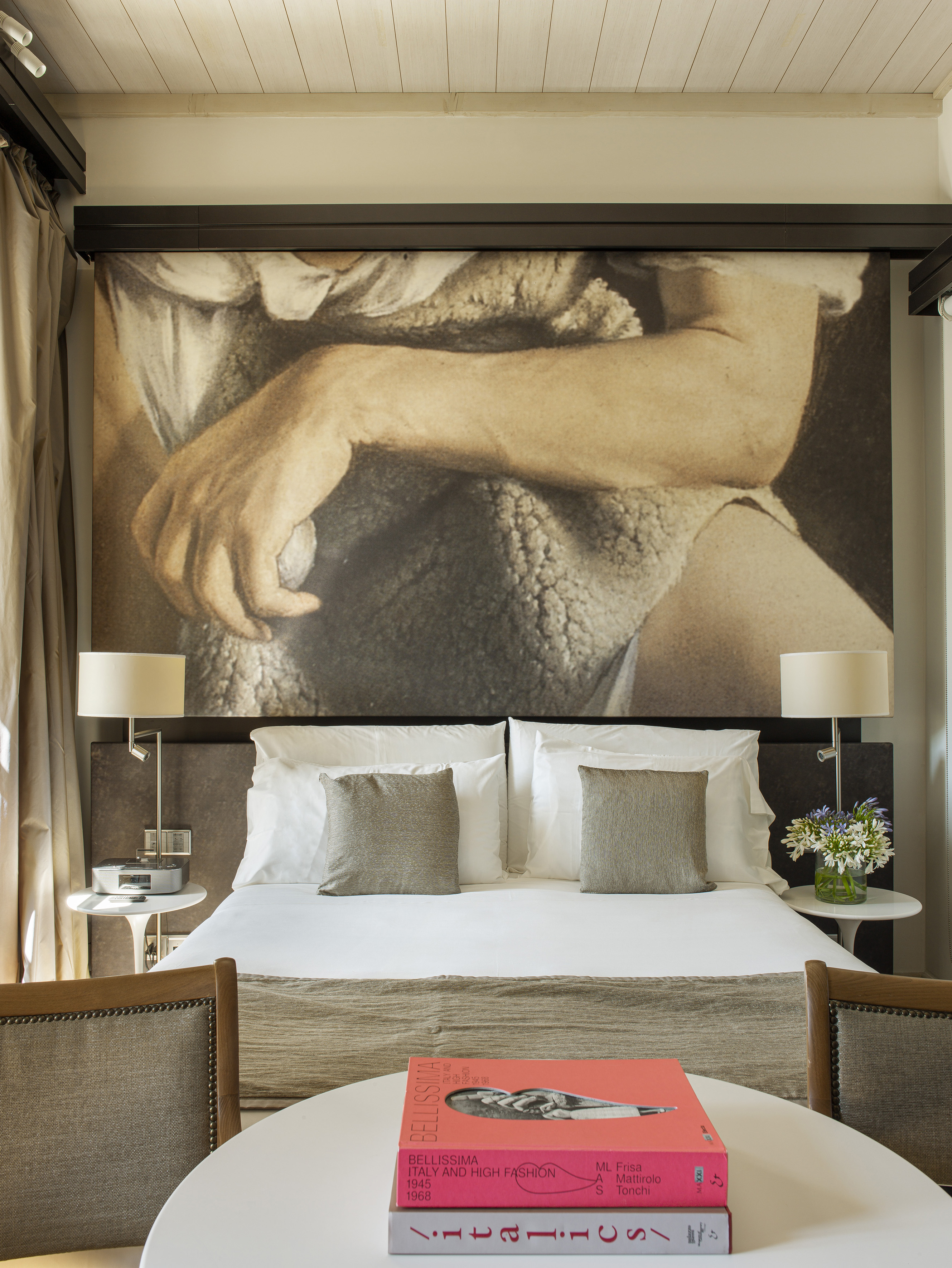 Stylish bedroom with bed, large art mural, bedside lamps, and fashion book.
