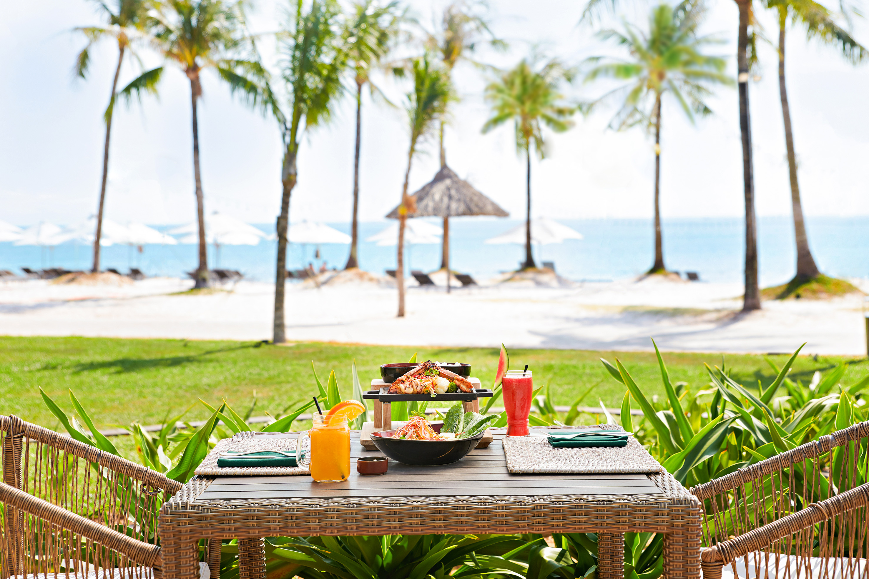 Beachfront dining with seafood, drinks, palm trees, and ocean view.