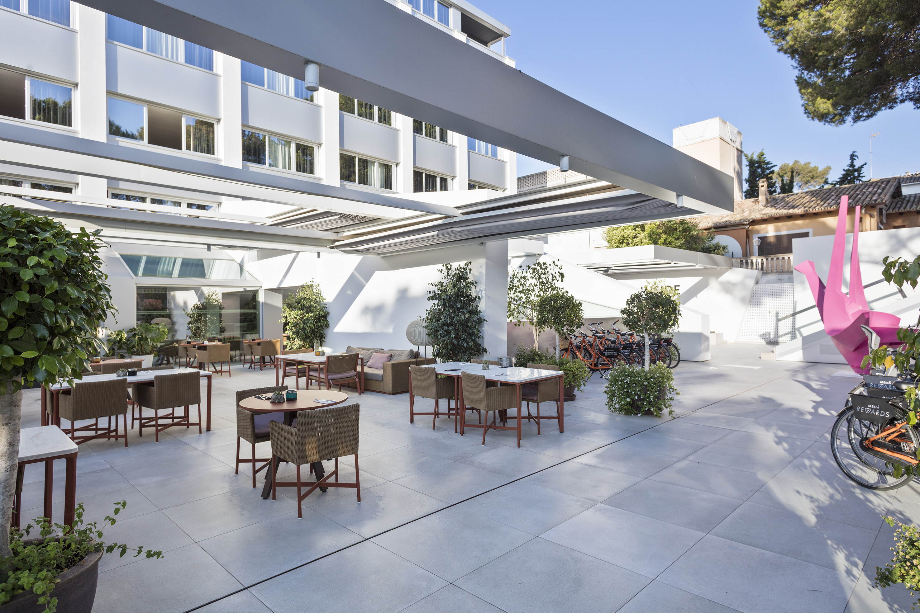 Modern hotel outdoor terrace with dining sets, green plants, and rental bikes.