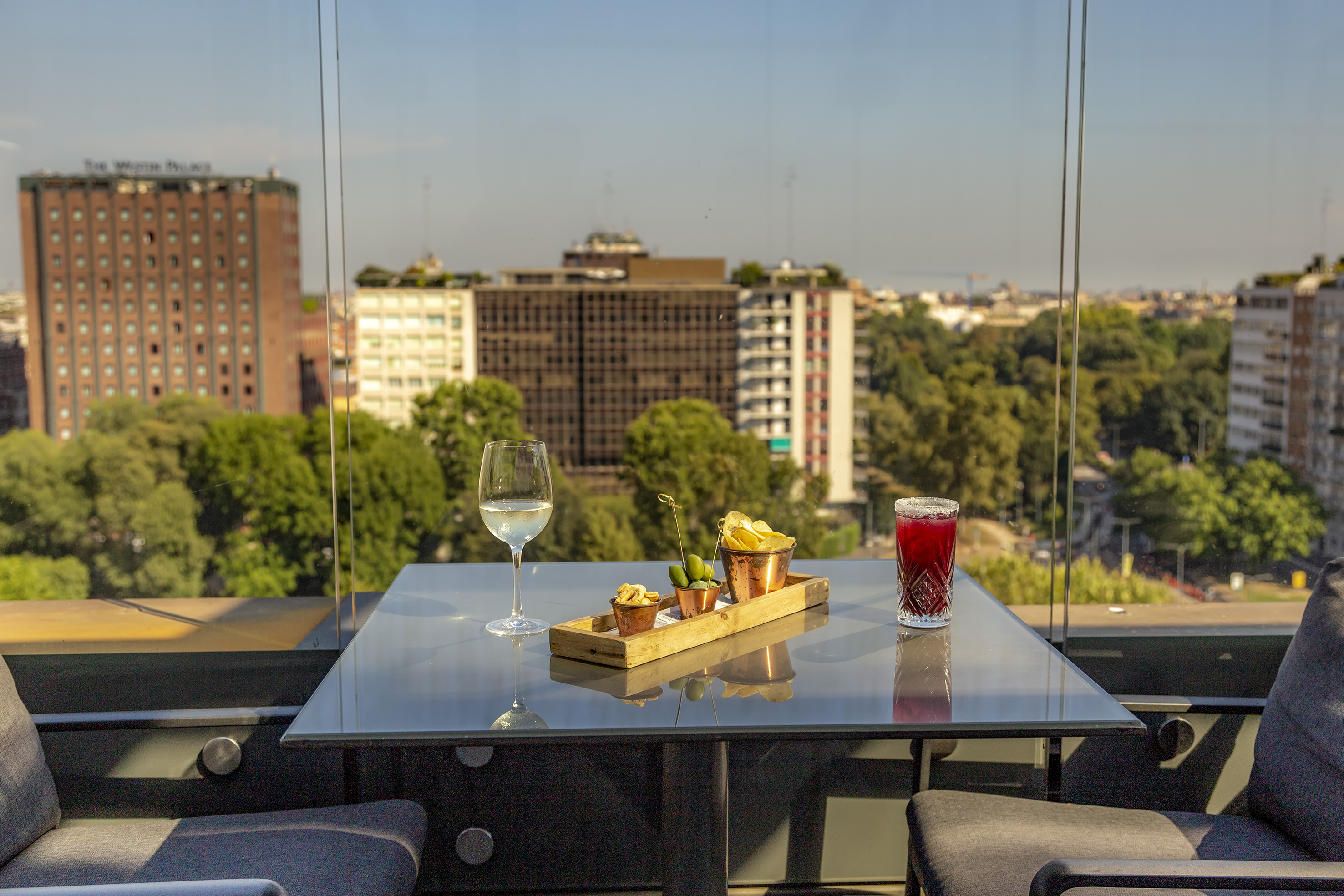Rooftop aperitivo with wine, cocktail, snacks, and panoramic city view.