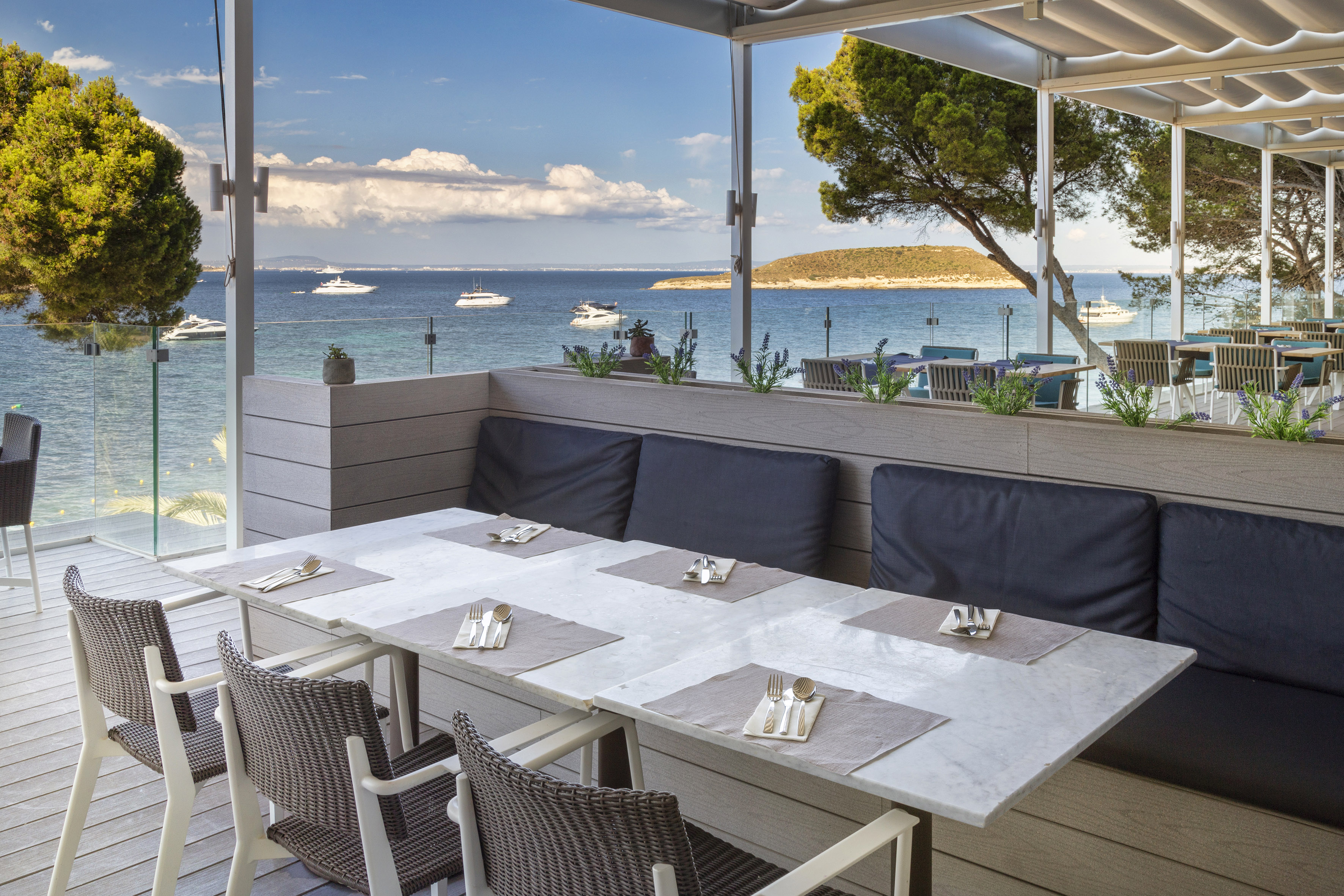 Outdoor restaurant terrace with sea view, yachts, and set dining tables.