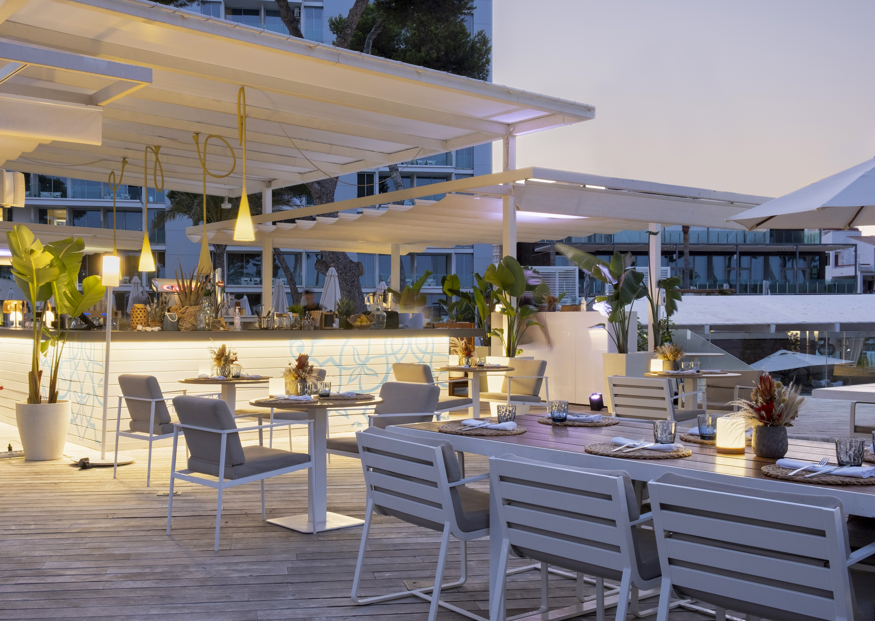 Modern outdoor restaurant terrace with tables, bar, and ambient evening lighting.