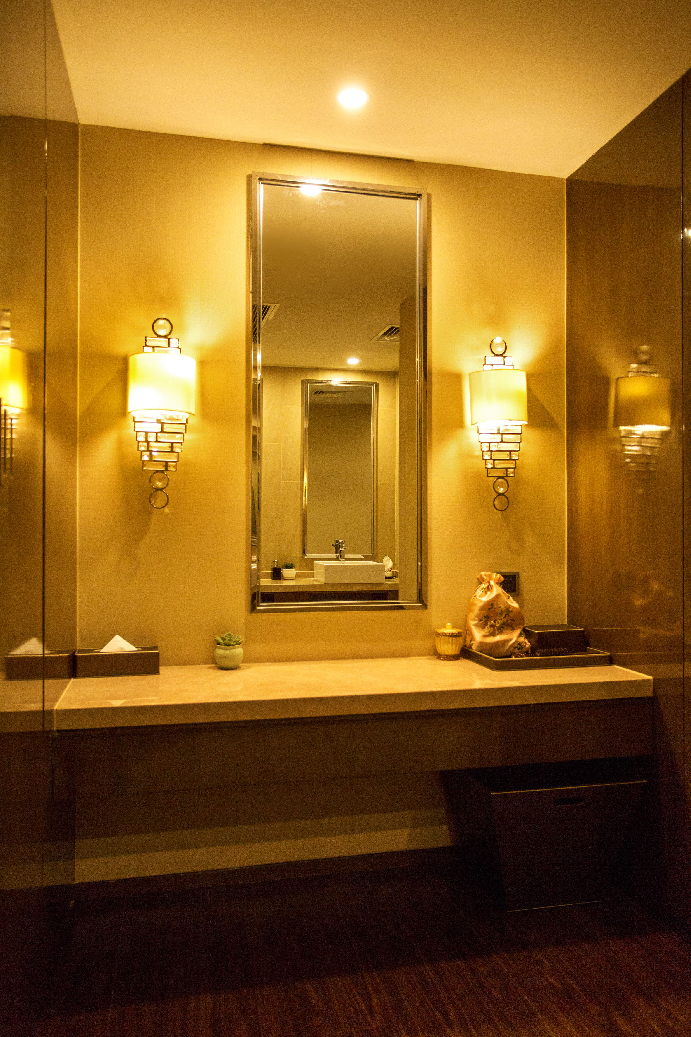 Warmly lit hotel bathroom vanity with mirror and decorative wall sconces.