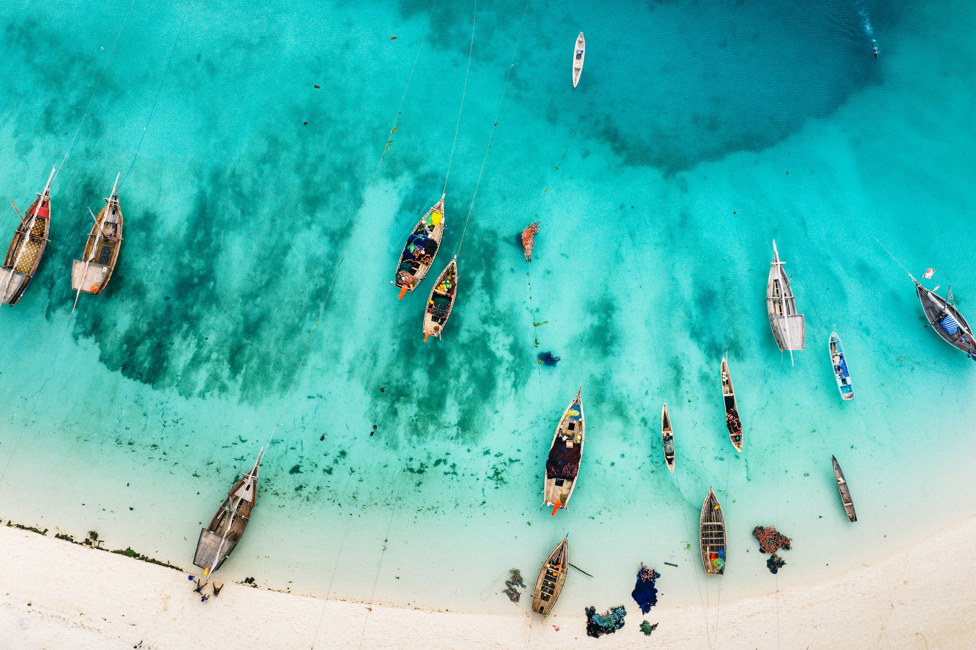 Vista aérea: barcos de pesca tradicionales en playa tropical de agua turquesa.