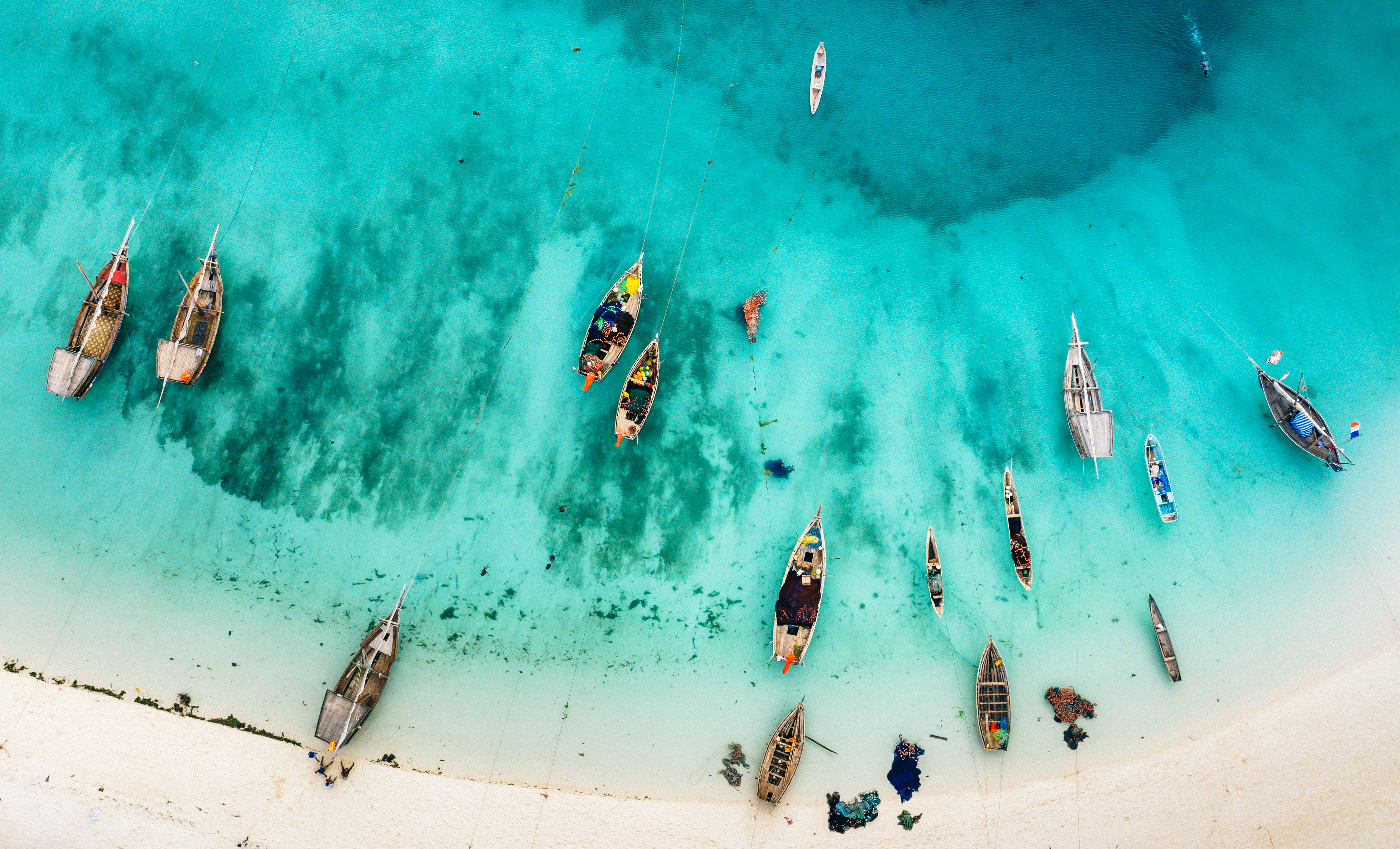 Vista aérea: barcos de pesca tradicionales en playa tropical de agua turquesa.