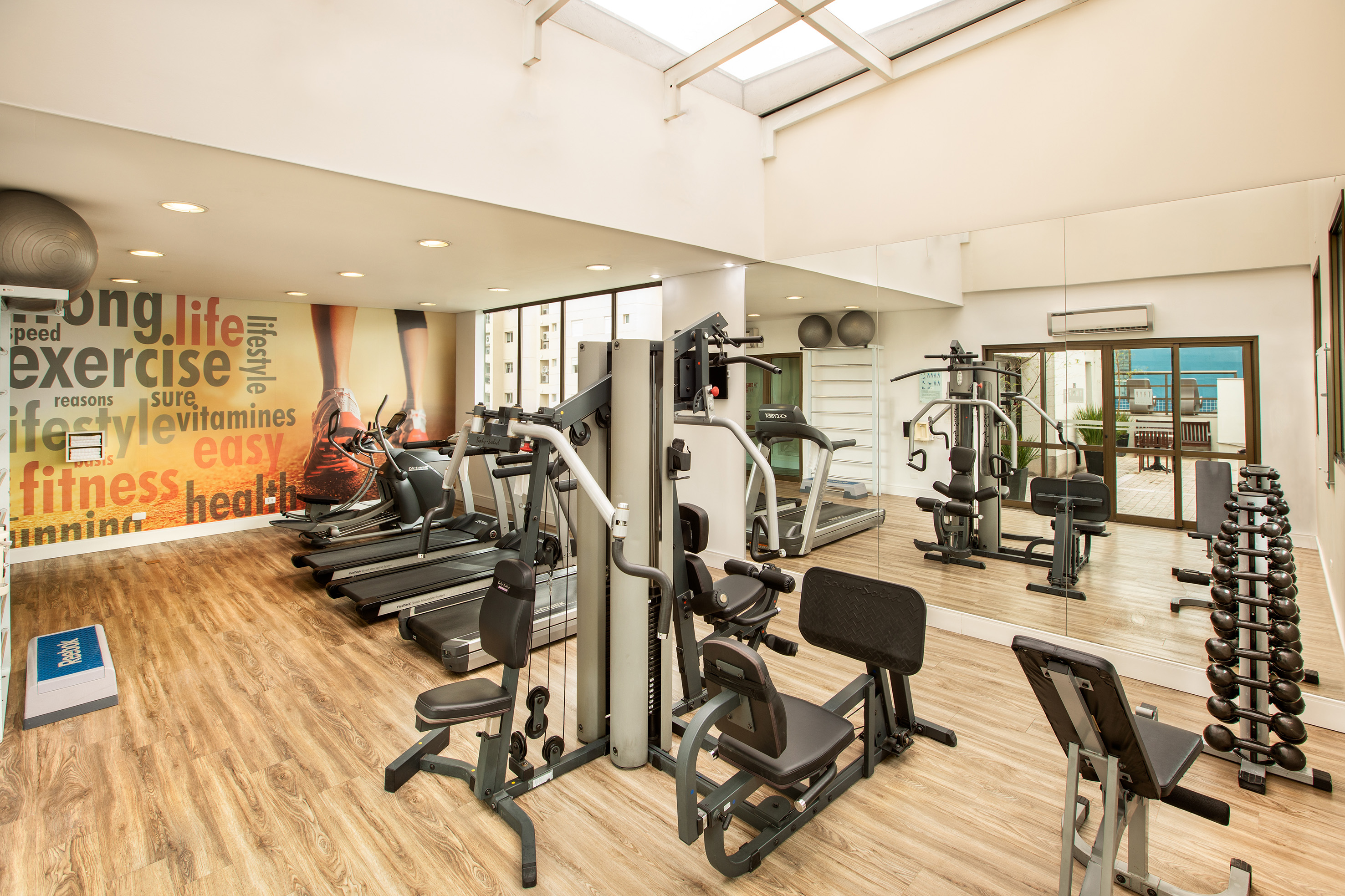 Gym with fitness equipment, treadmills, weight machines, dumbbells, and mural.