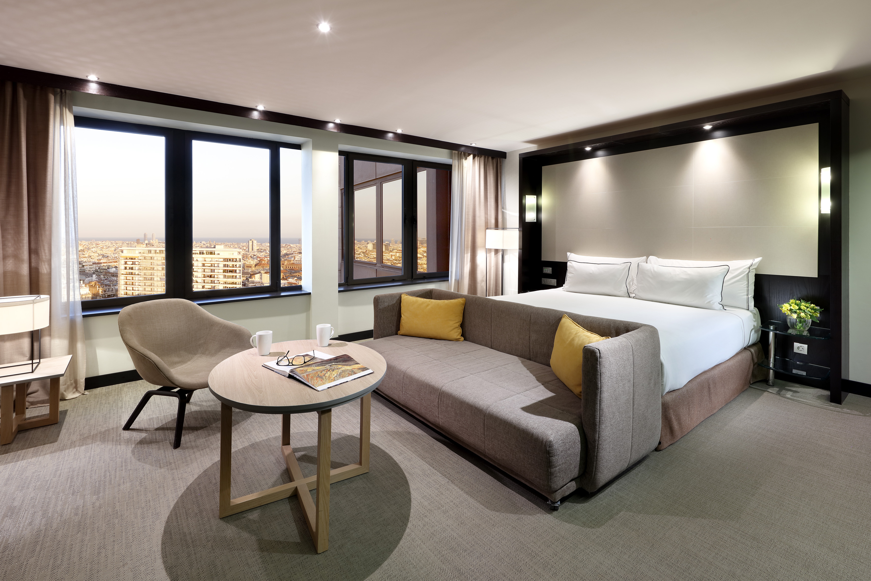 Elegant hotel suite with king bed, modern sofa, and expansive city views.