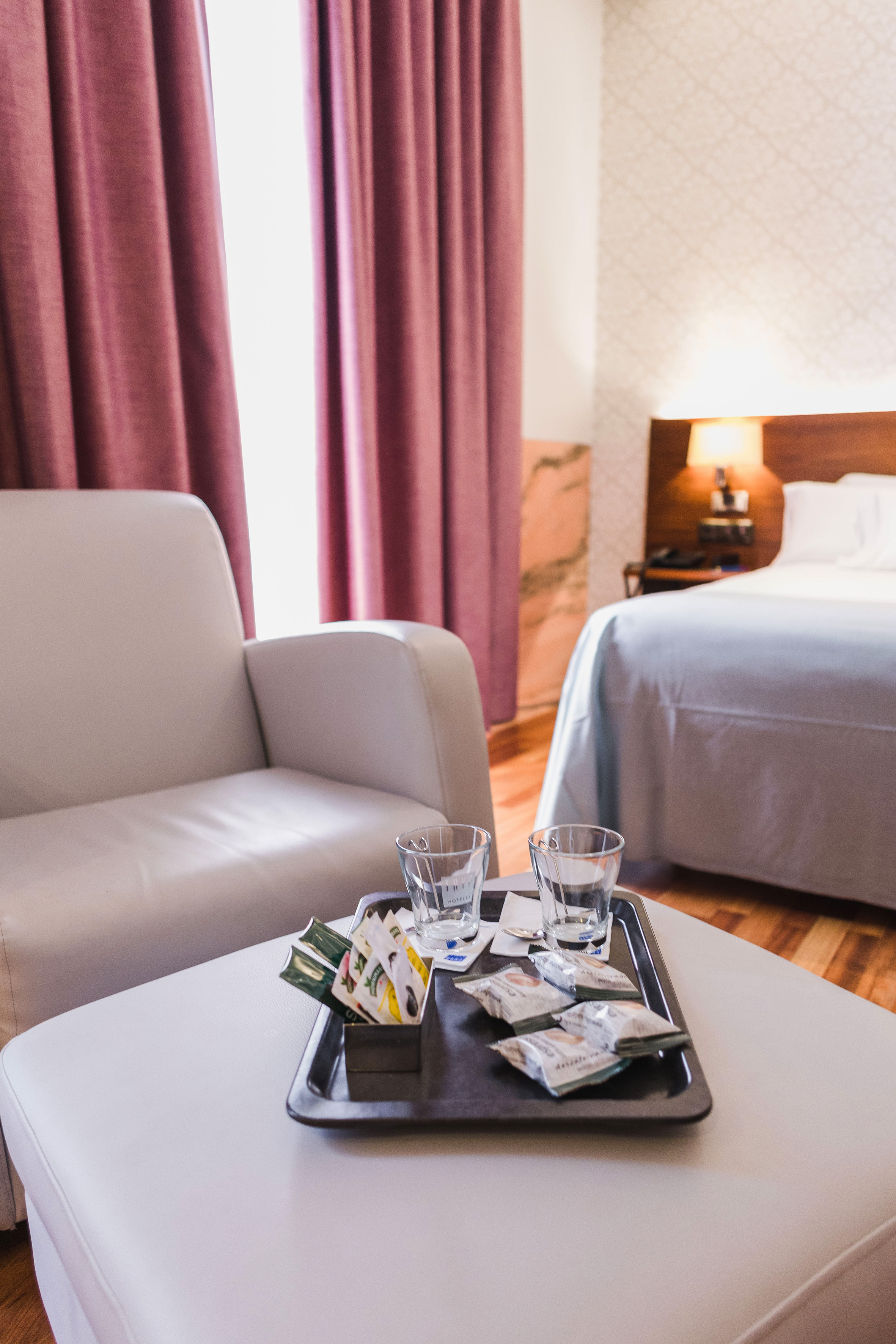 Hotel room amenities: coffee/tea tray on ottoman, armchair, and bed.