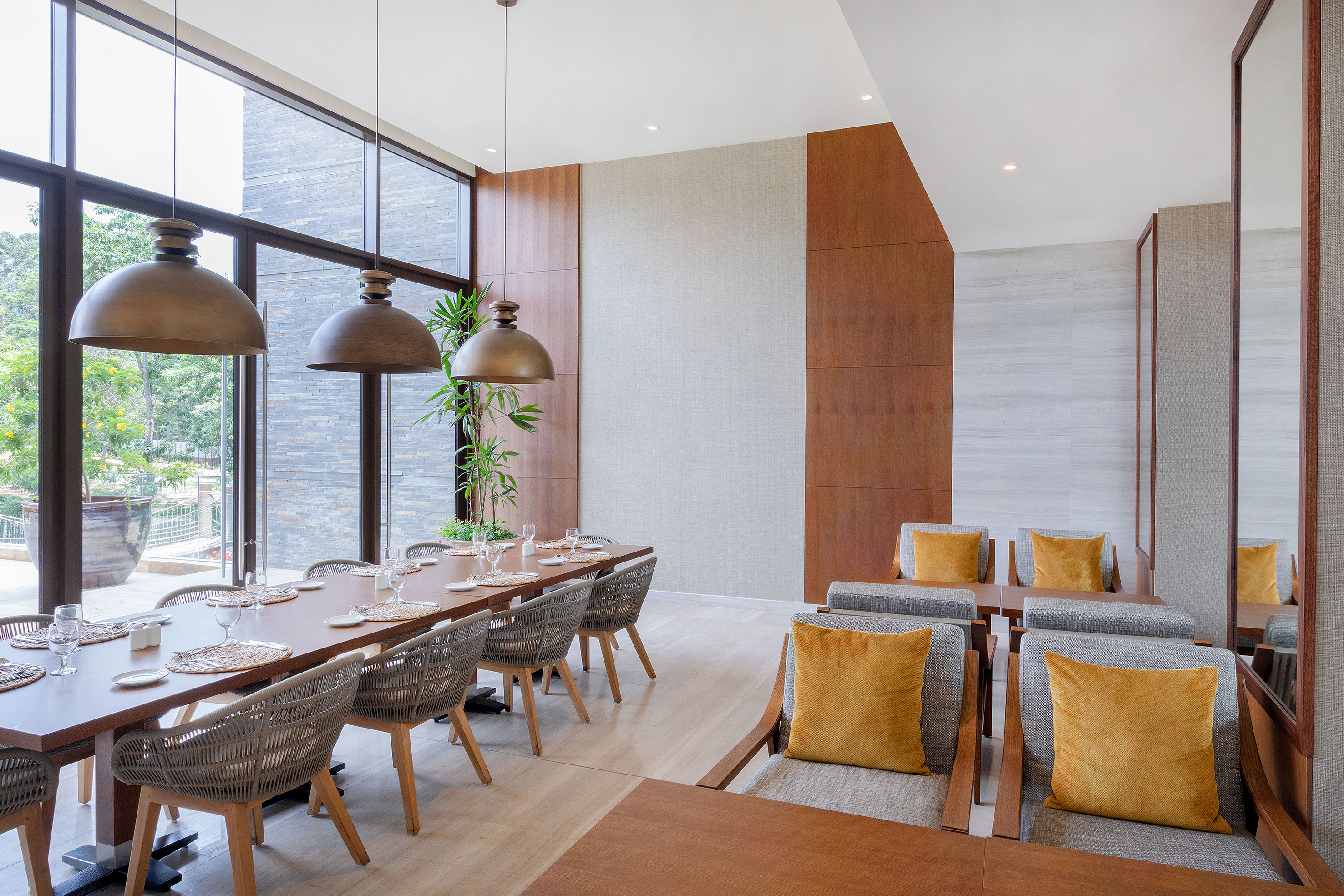 Elegant restaurant interior: long dining table, woven chairs, large windows, lounge.