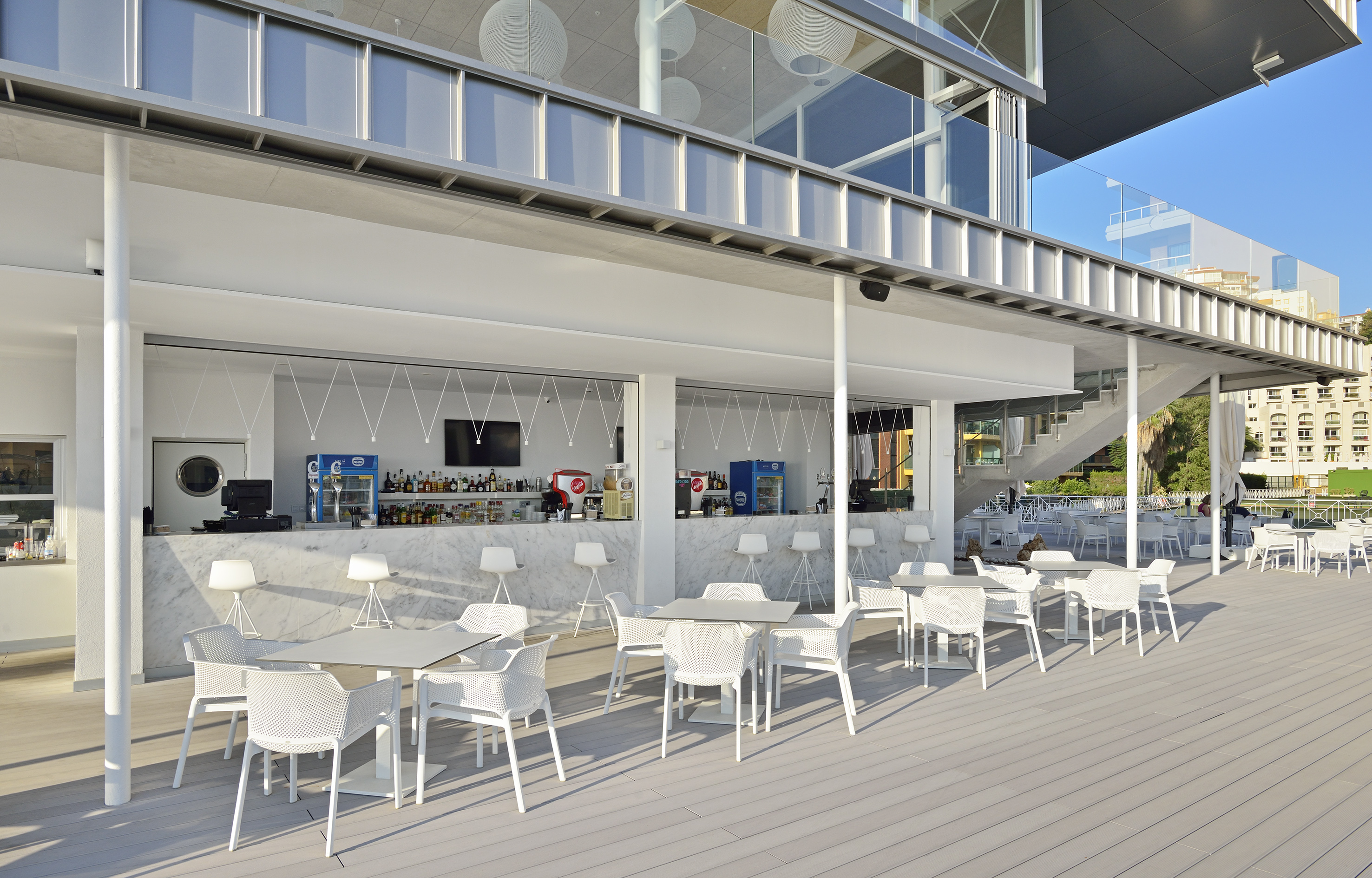 Modern outdoor bar terrace with white furniture and marble counter on deck.
