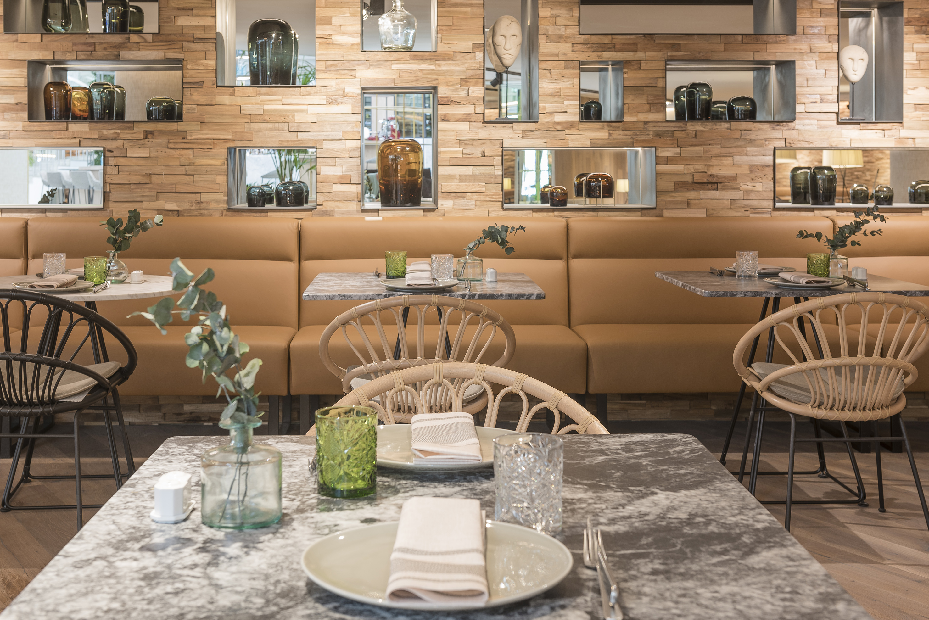 Modern restaurant dining interior with wood wall, booth seating, and marble tables.