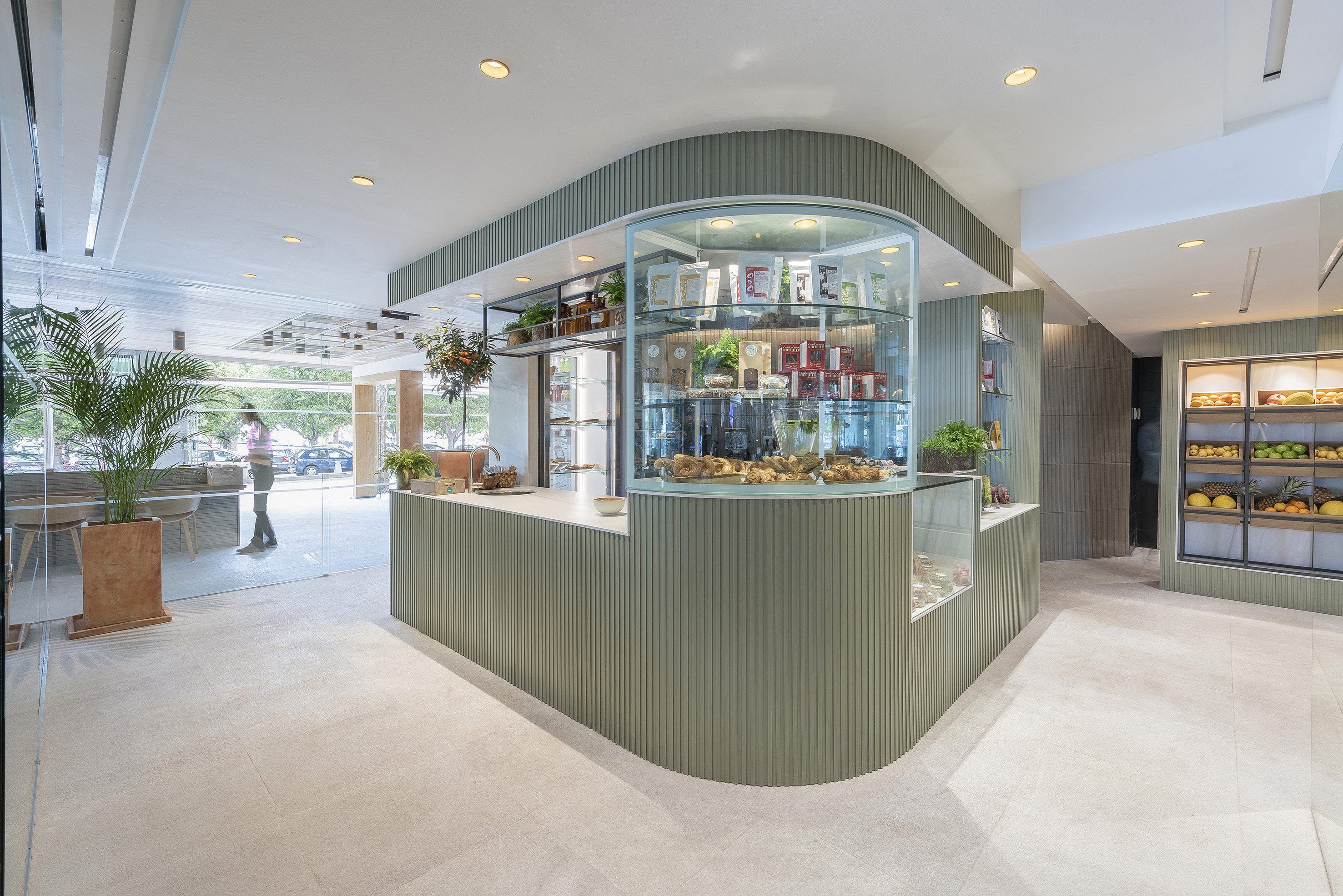 Curved sage green fluted cafe counter with pastries and fresh fruit display.