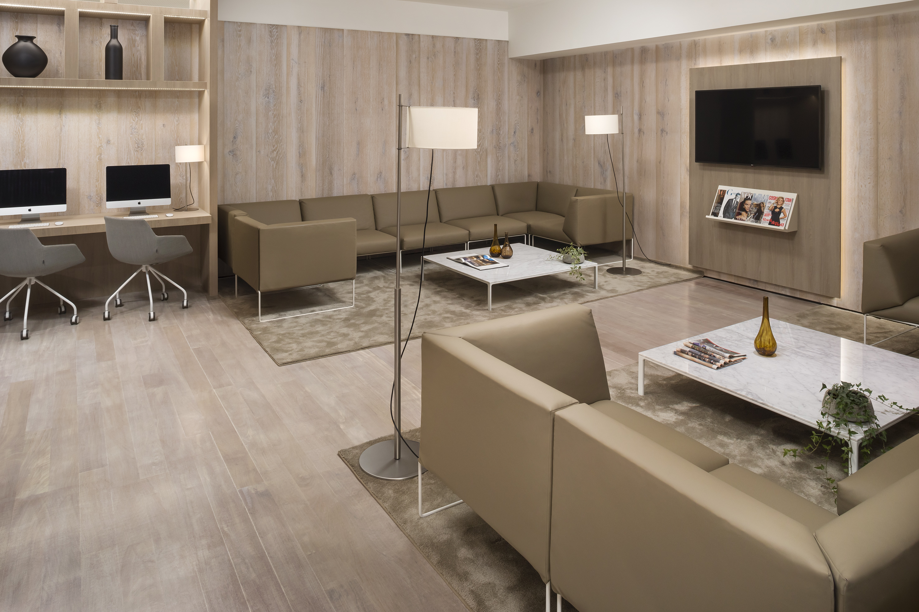 Modern office lounge with beige sectional sofas, computer workstations, and wood paneling.