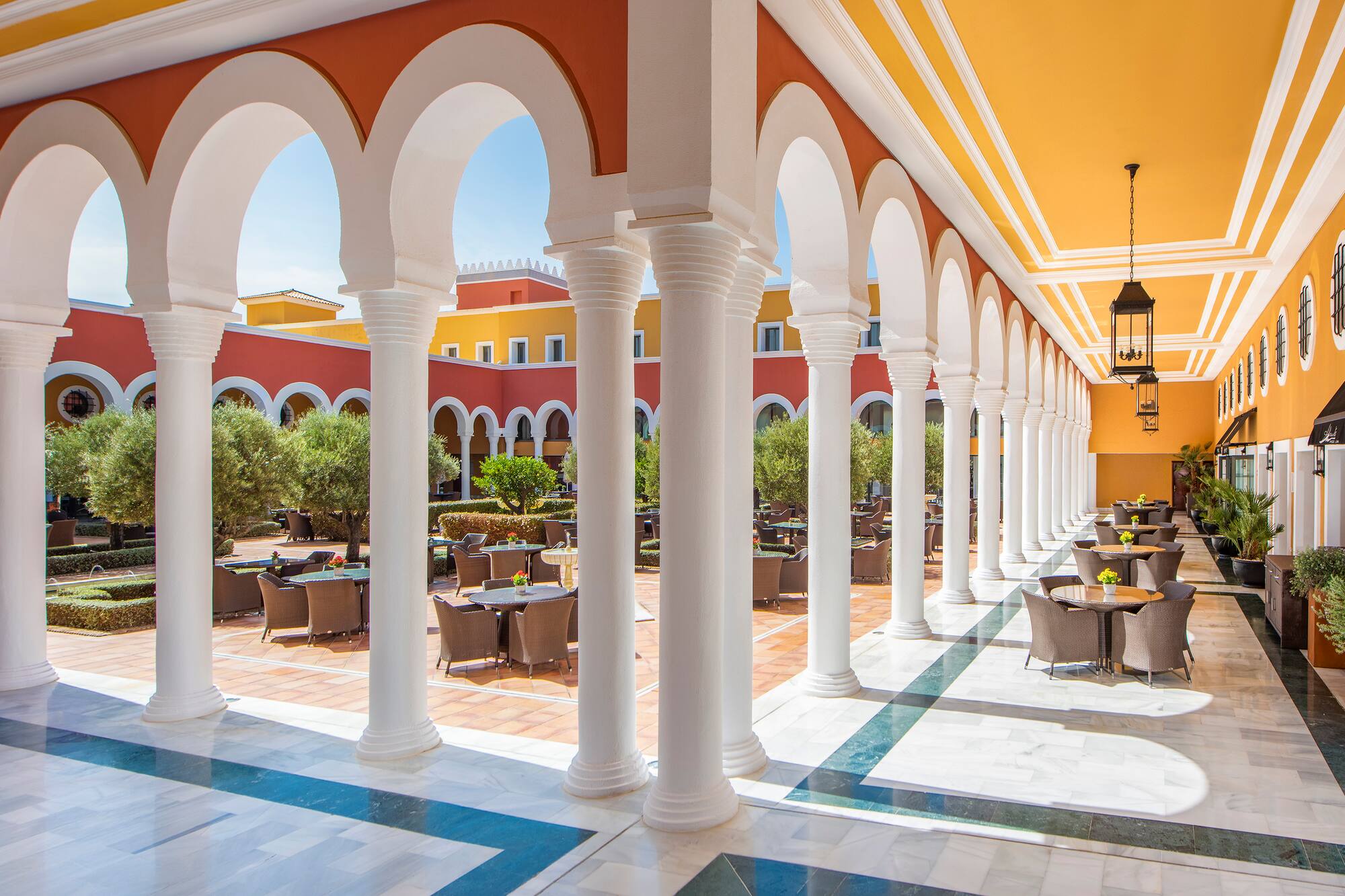 Sunny Mediterranean courtyard restaurant with arches, columns, and outdoor seating.