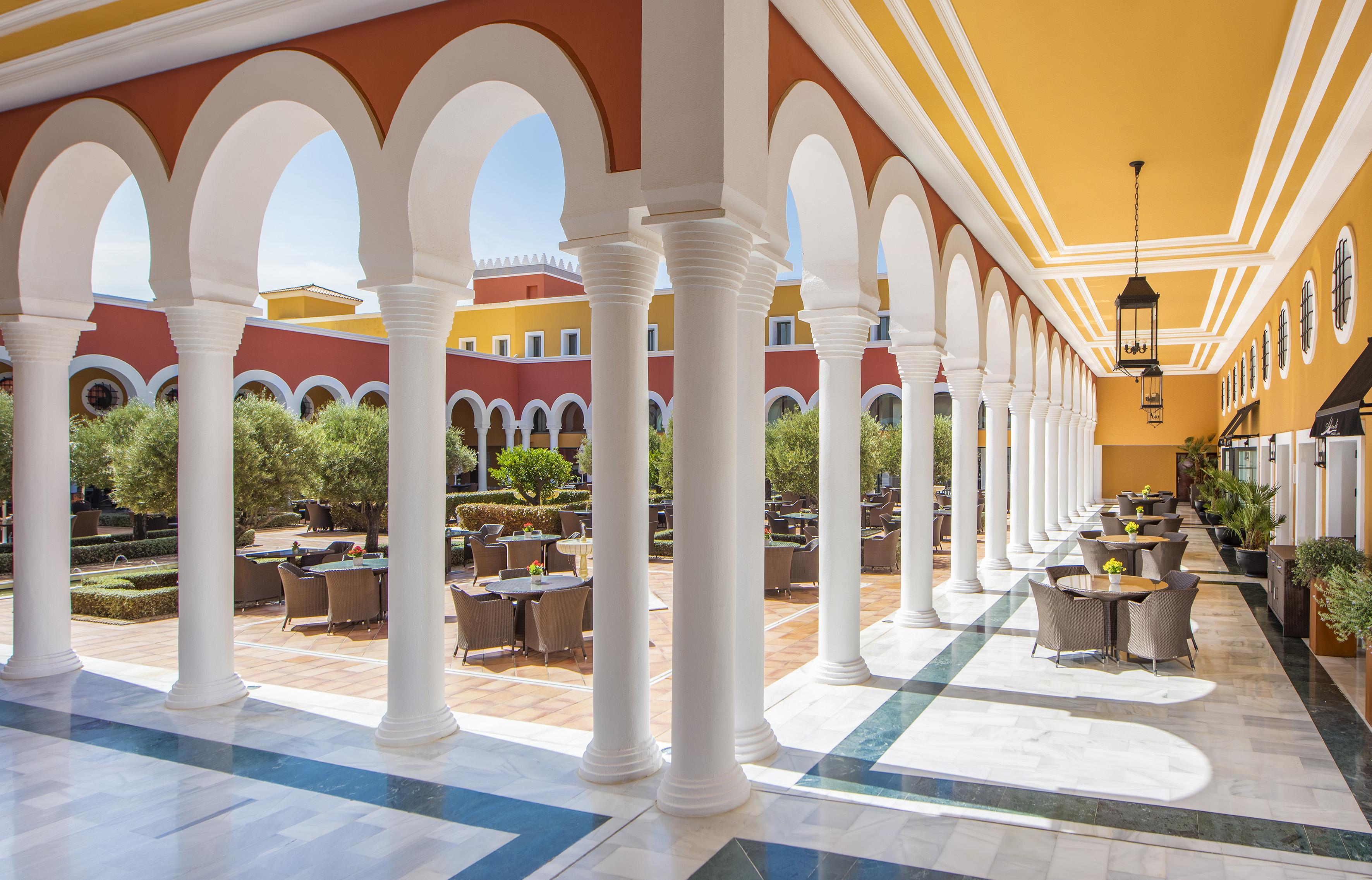 Sunny Mediterranean courtyard restaurant with arches, columns, and outdoor seating.