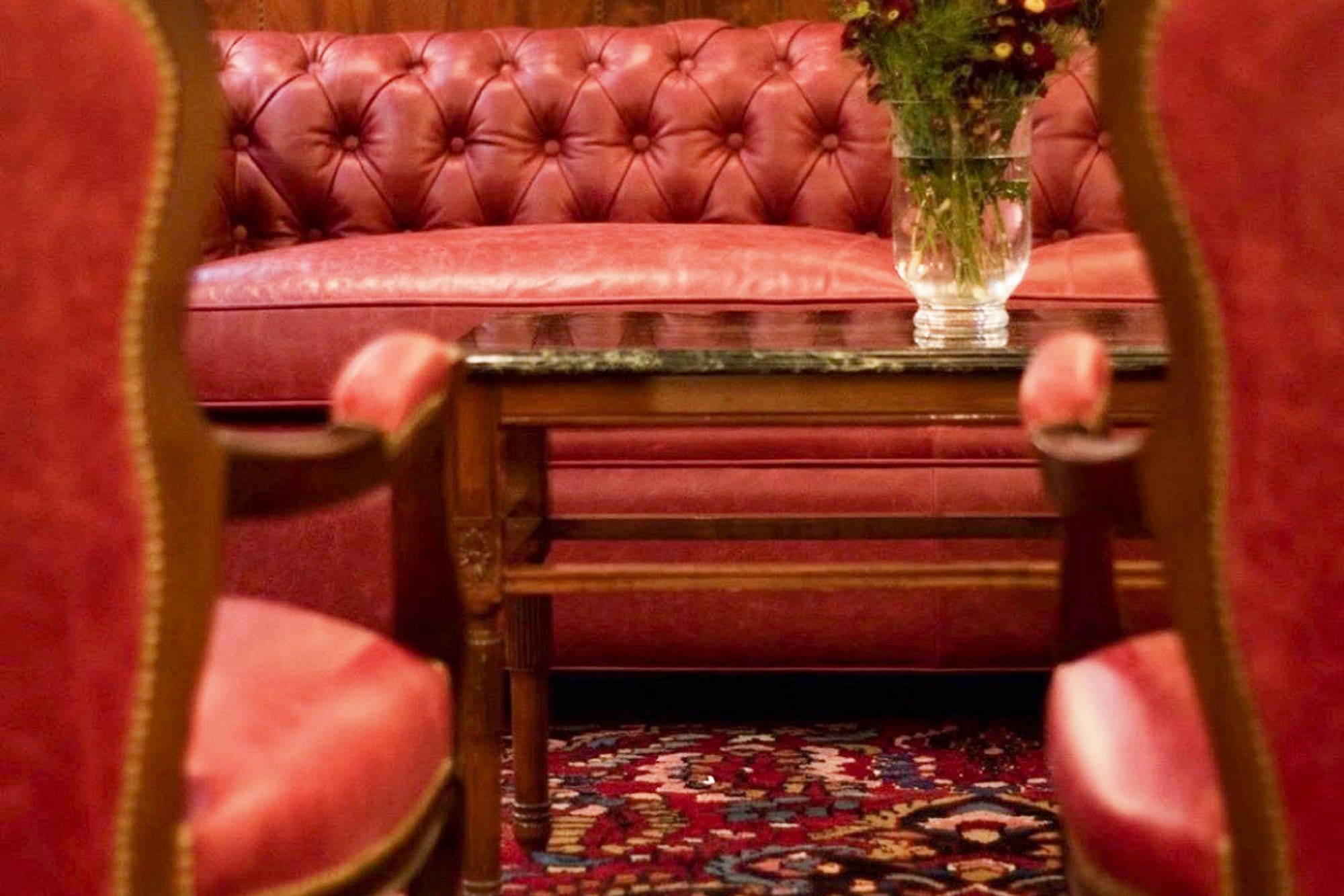Red leather tufted sofa, armchairs, coffee table with flowers, ornate rug.