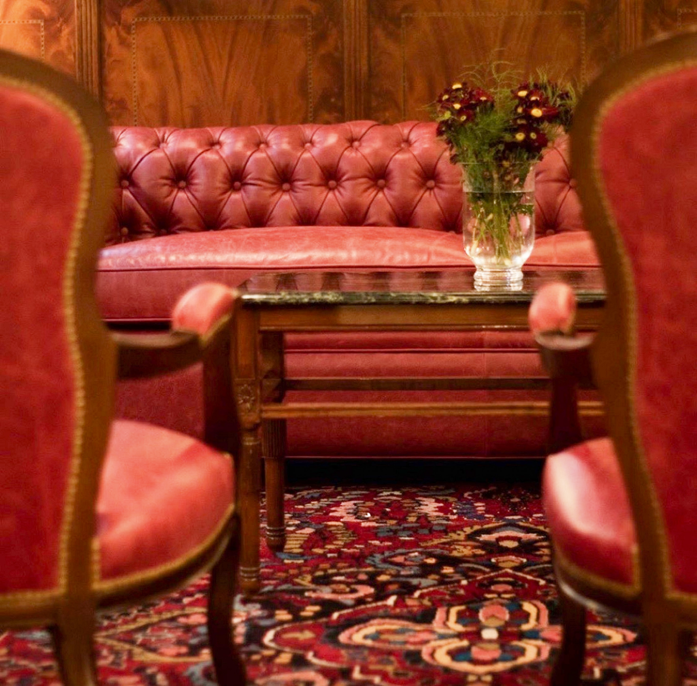 Red leather tufted sofa, armchairs, coffee table with flowers, ornate rug.