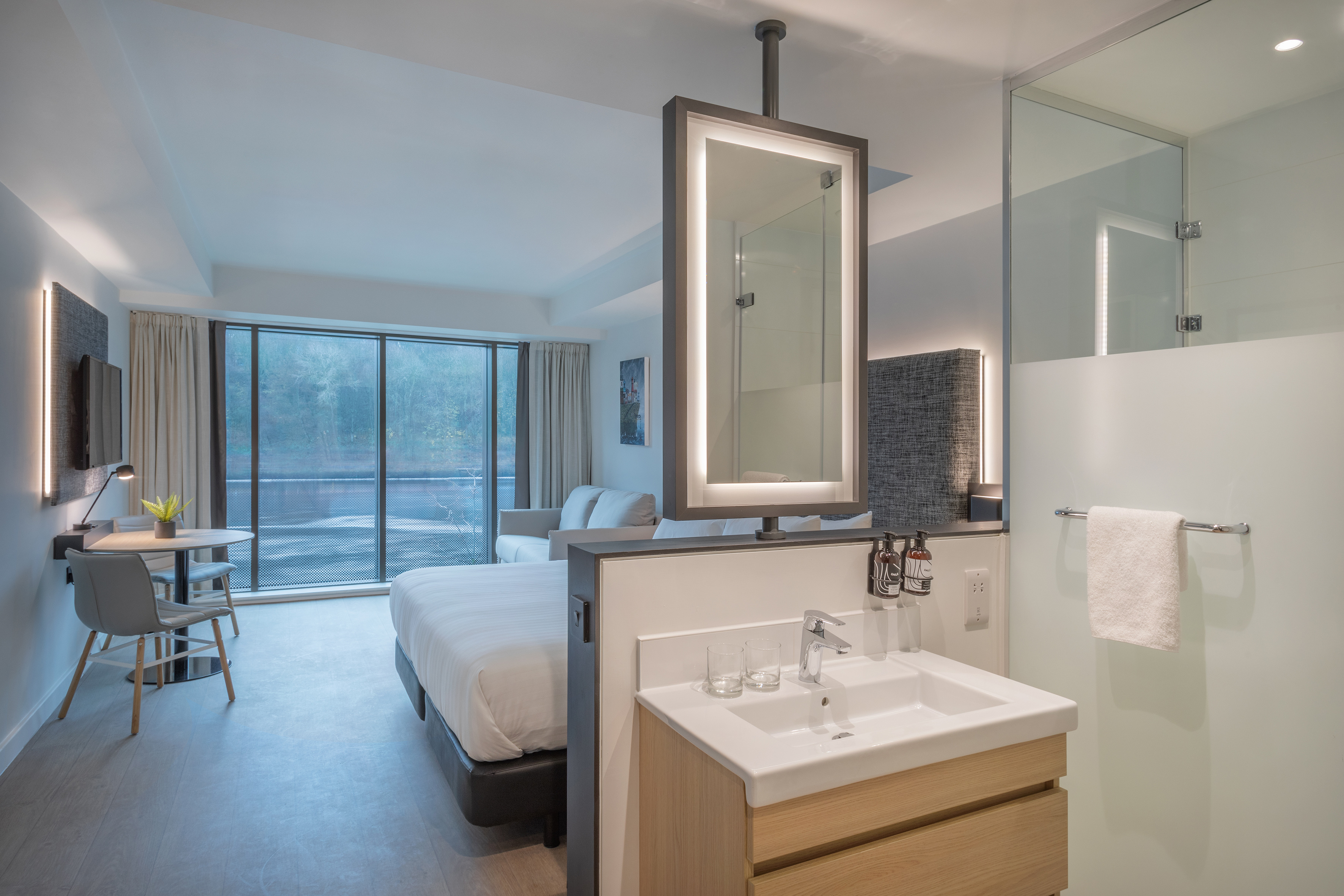 Modern hotel room with bed, large window view, and integrated bathroom vanity.