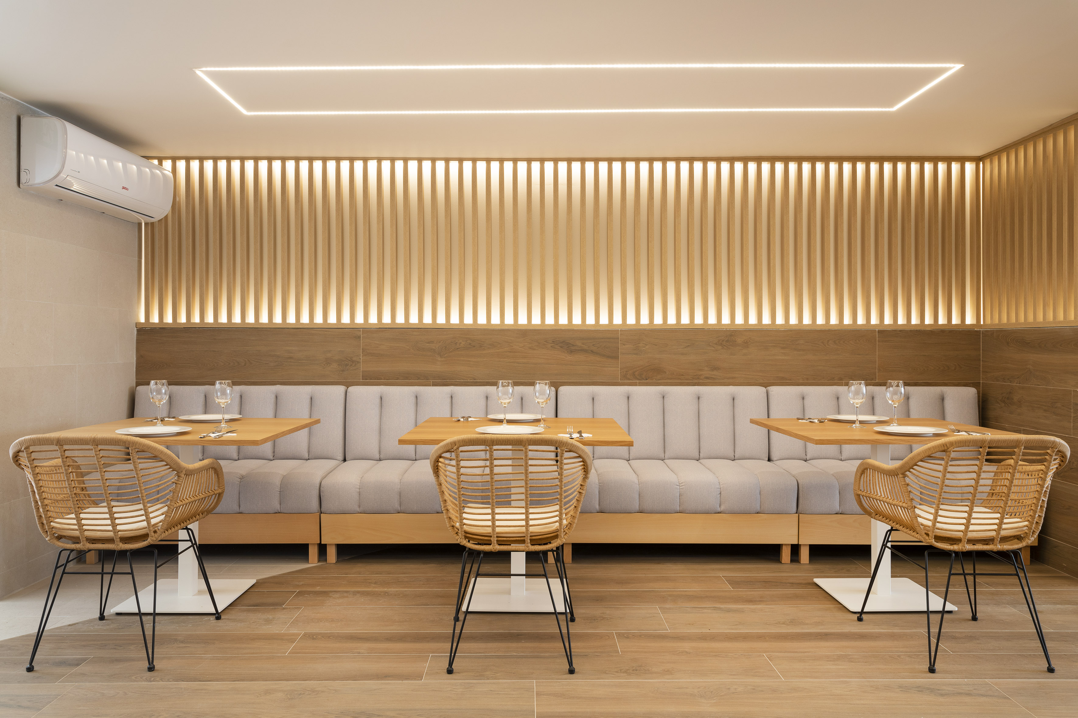 Modern restaurant interior with booth seating, wood tables, and illuminated slat wall.