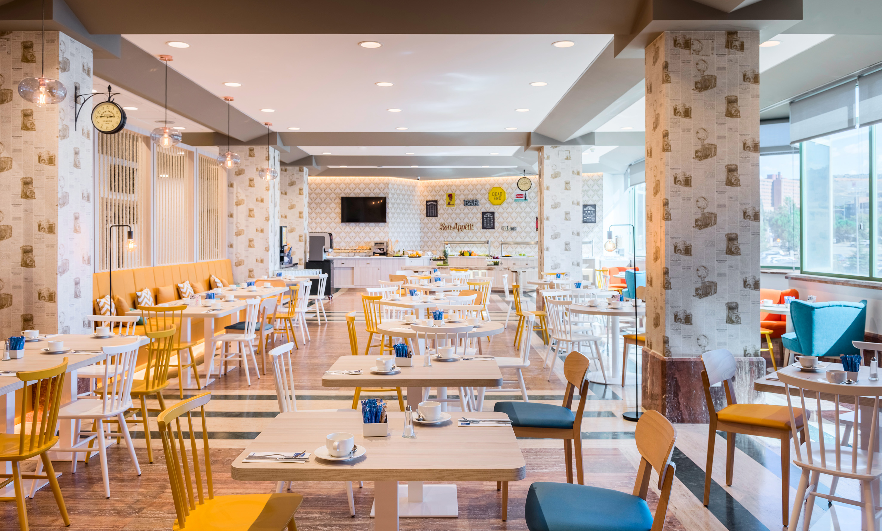Modern dining room with colorful chairs, breakfast buffet, and retro camera wallpaper.