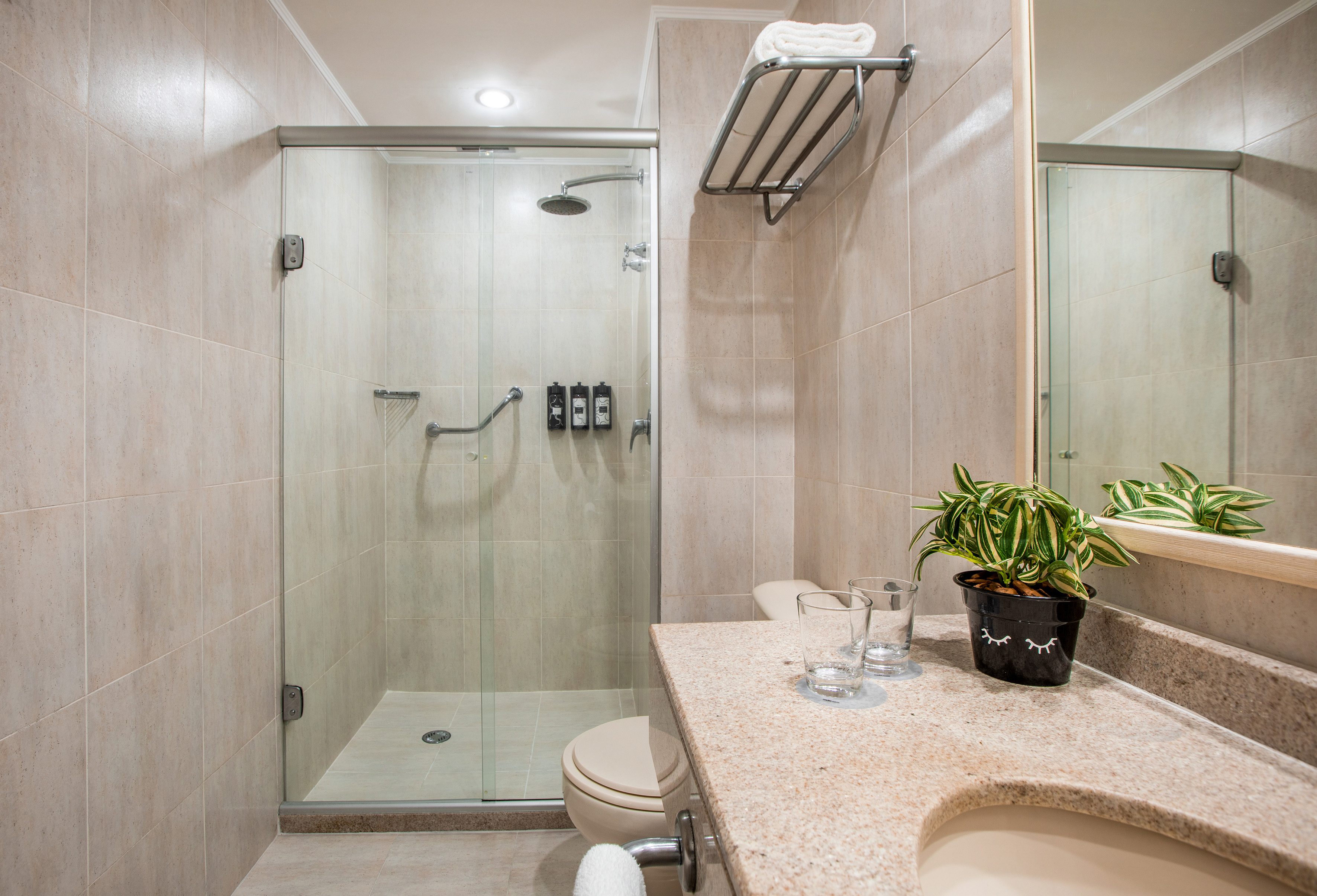 Modern bathroom with glass shower, toilet, granite vanity, and neutral tiles.