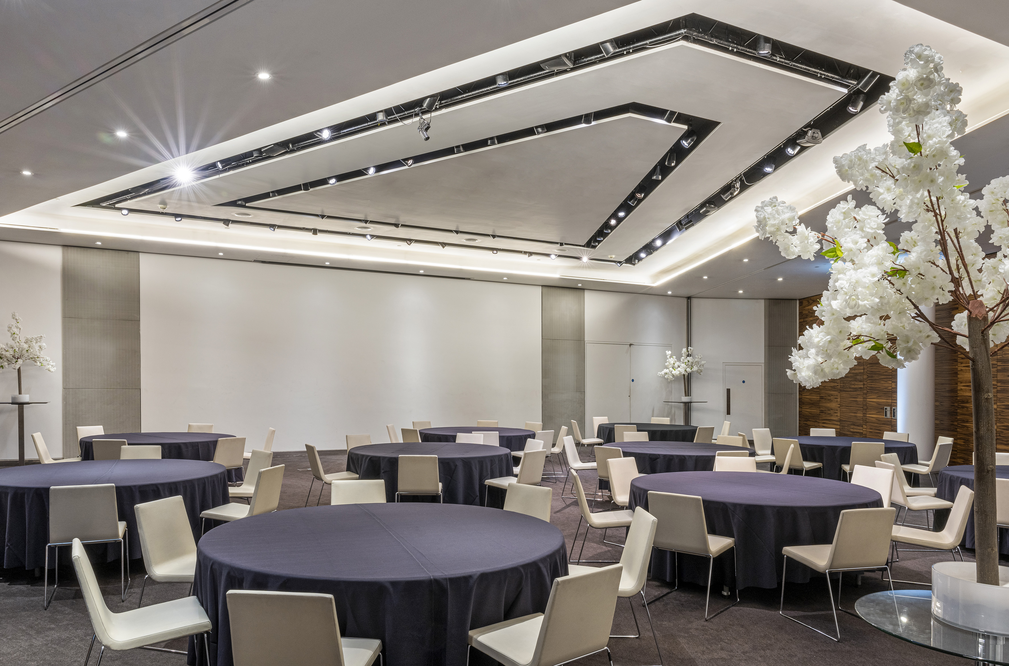 Modern ballroom with round tables, beige chairs, and cherry blossom decor.