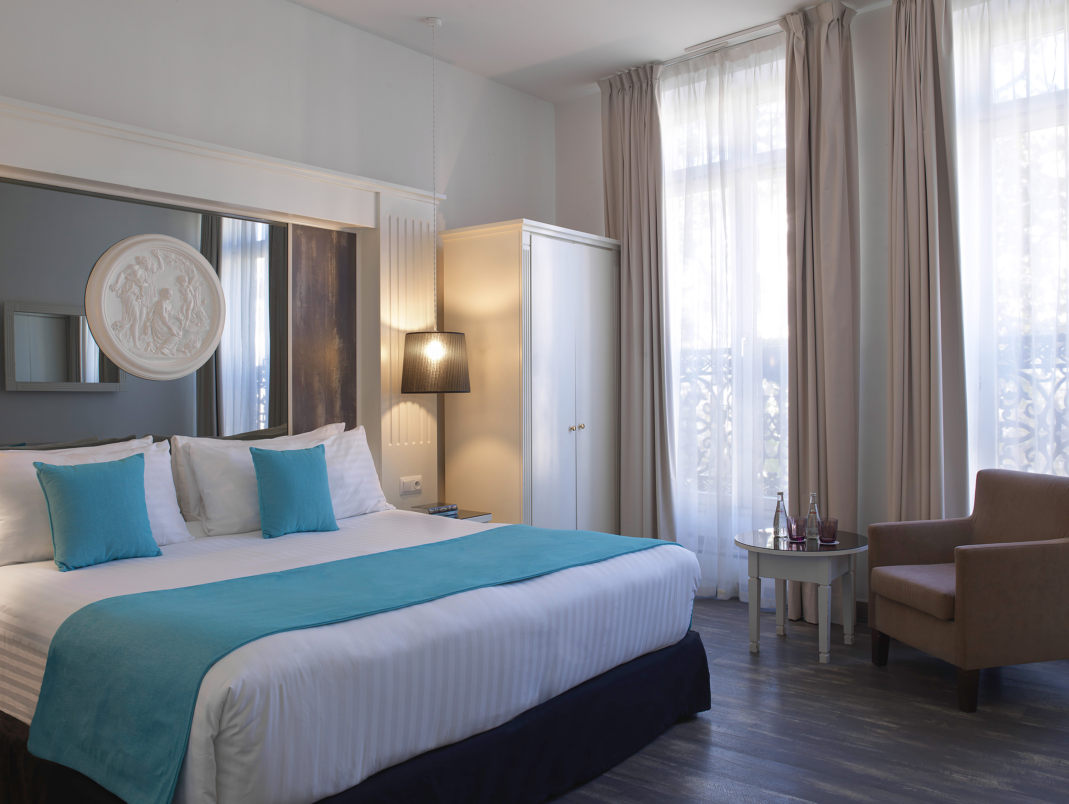 Modern hotel bedroom with king bed, blue accents, wardrobe, and natural light.