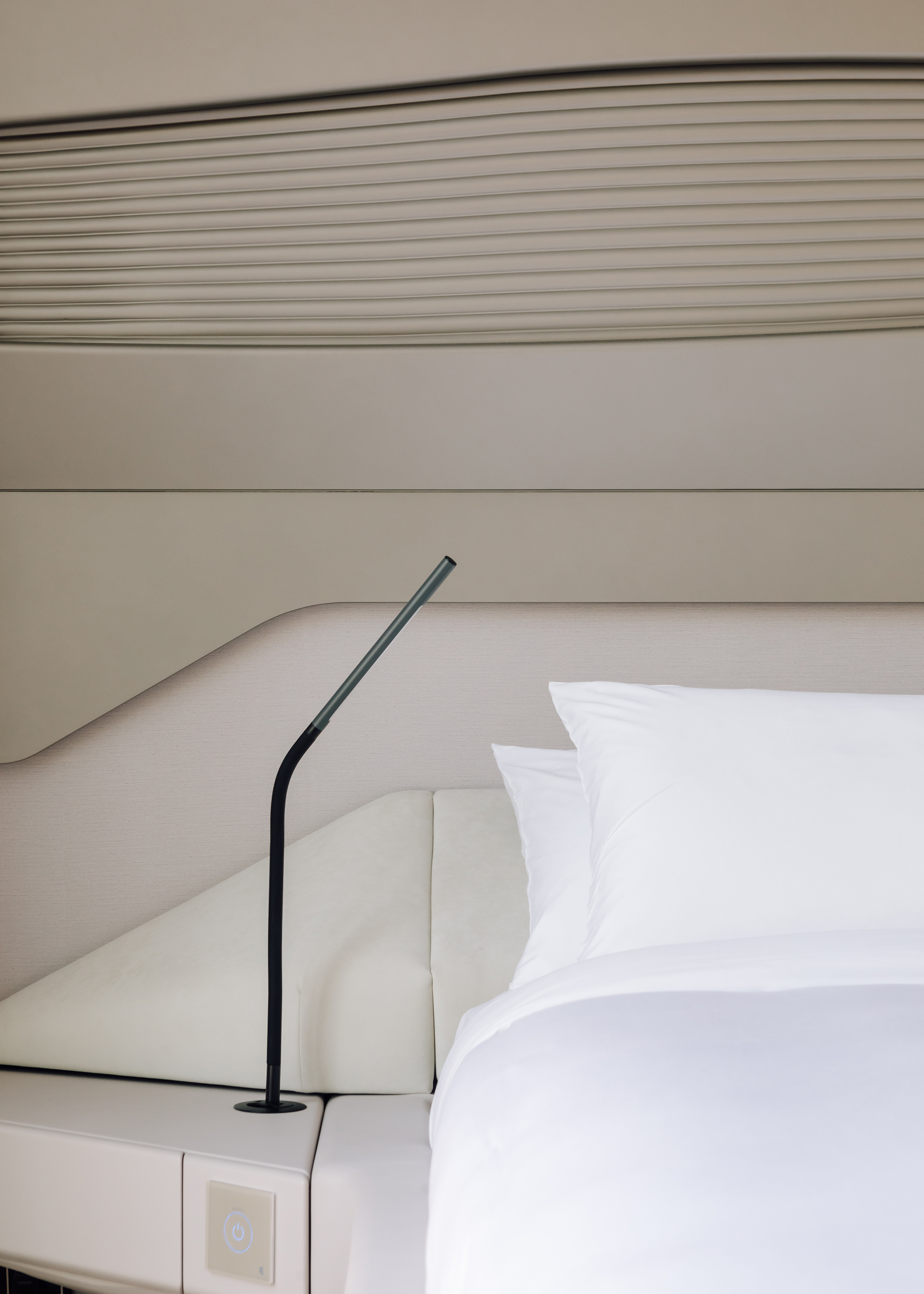 Minimalist hotel room with white bed, black reading lamp, and bedside controls.