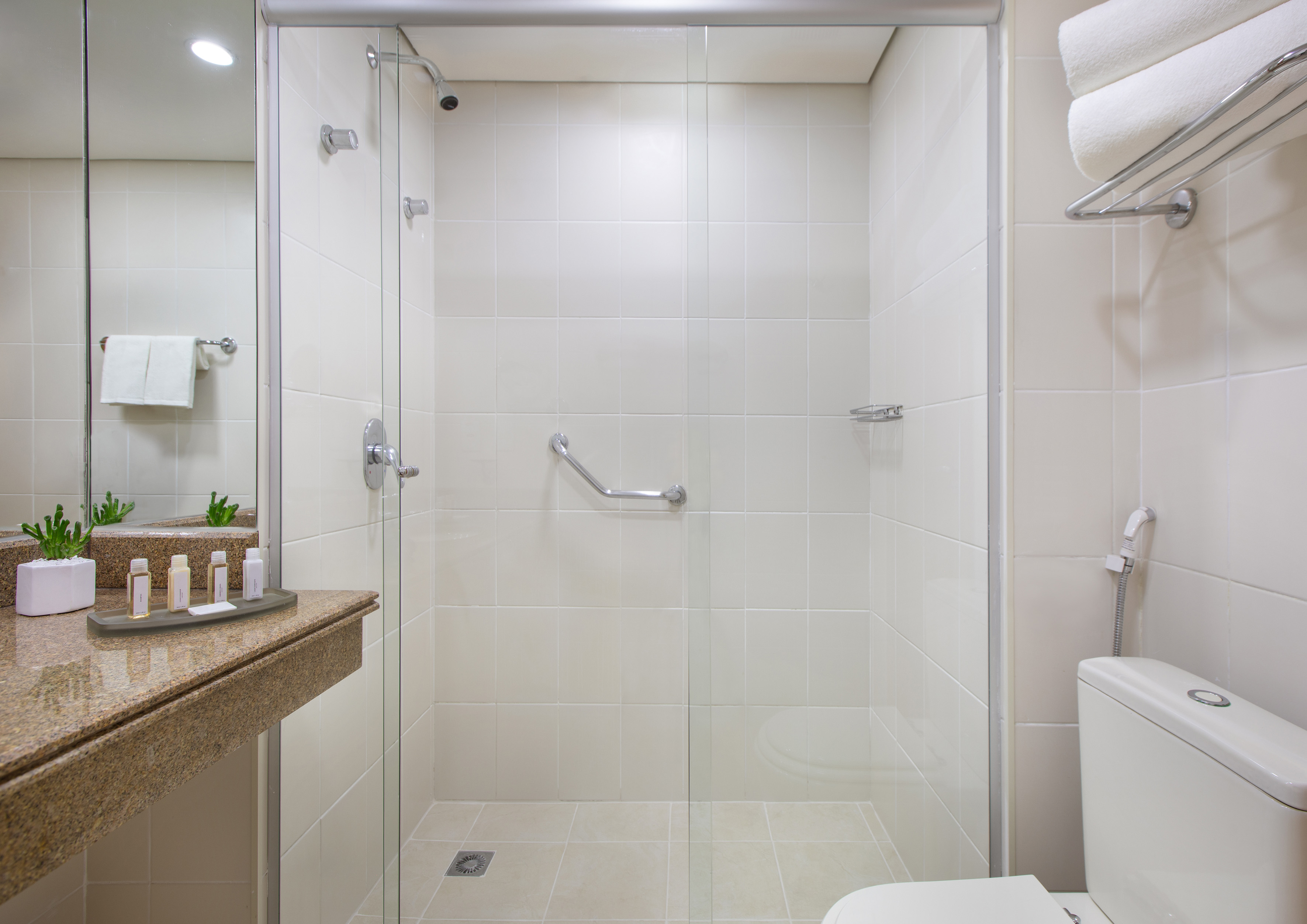 Modern hotel bathroom with glass shower, grab bar, vanity, and toilet.