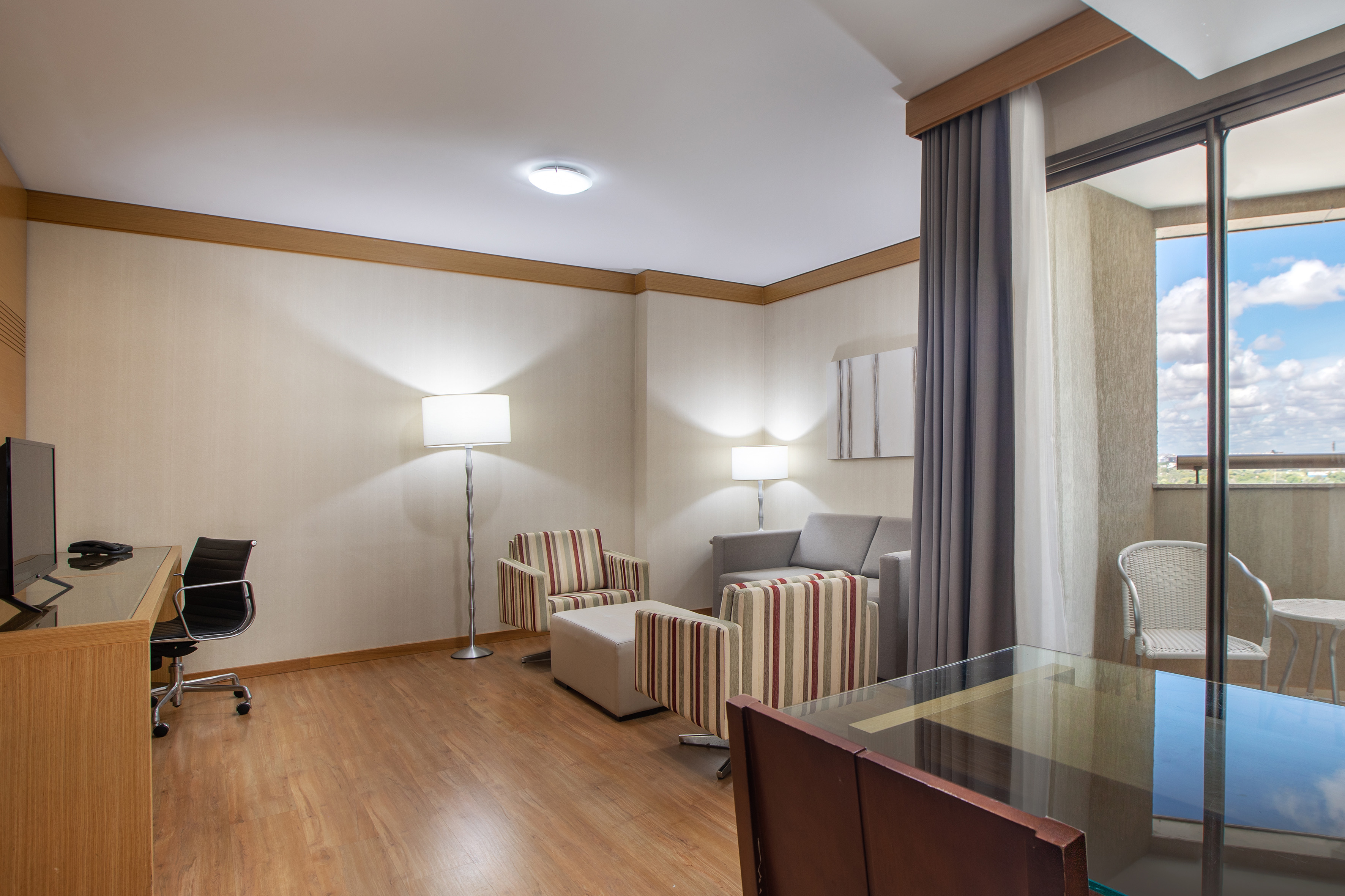 Spacious hotel suite with living area, work desk, and balcony access.