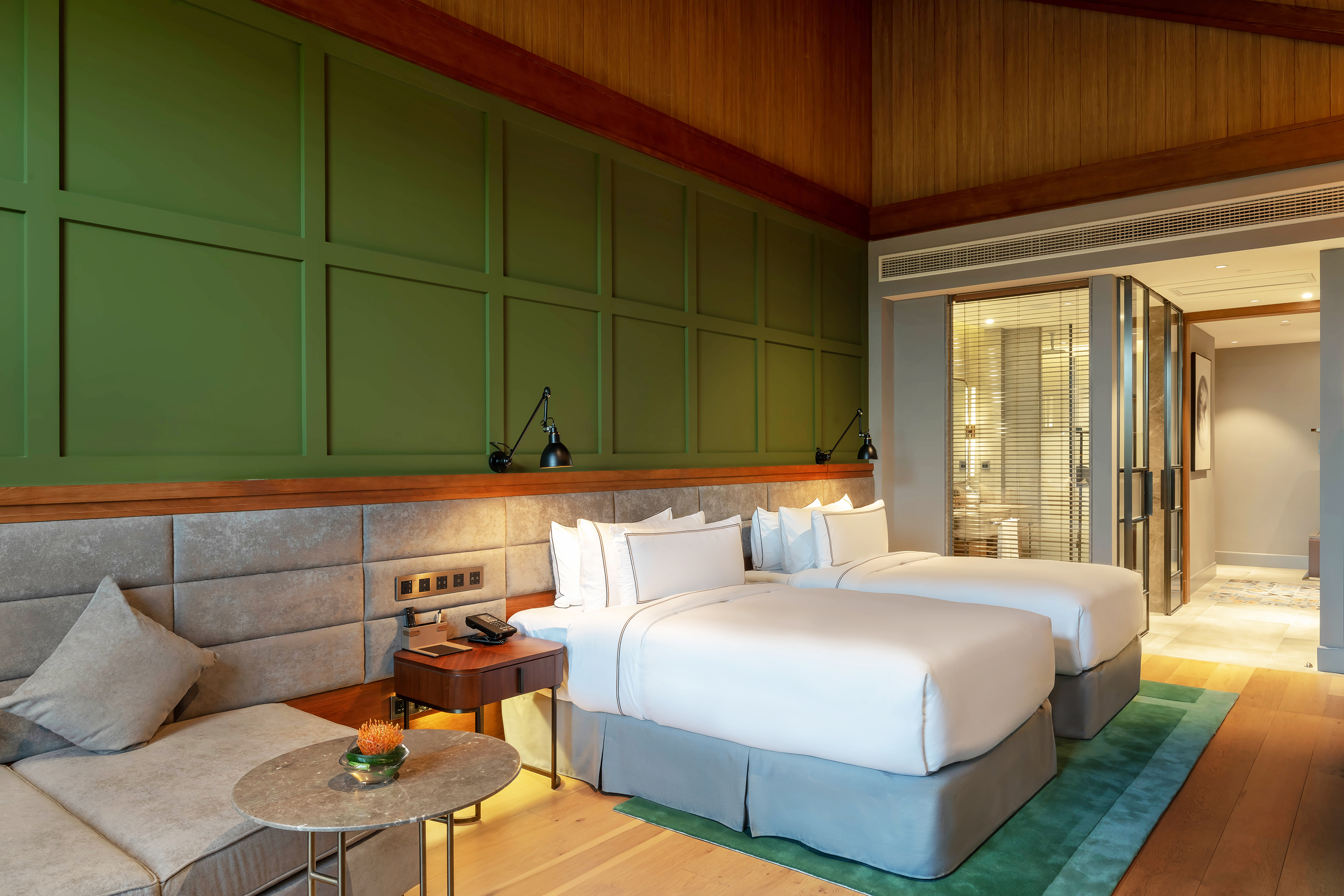 Stylish hotel bedroom with two twin beds, green wall paneling, and wooden ceiling.