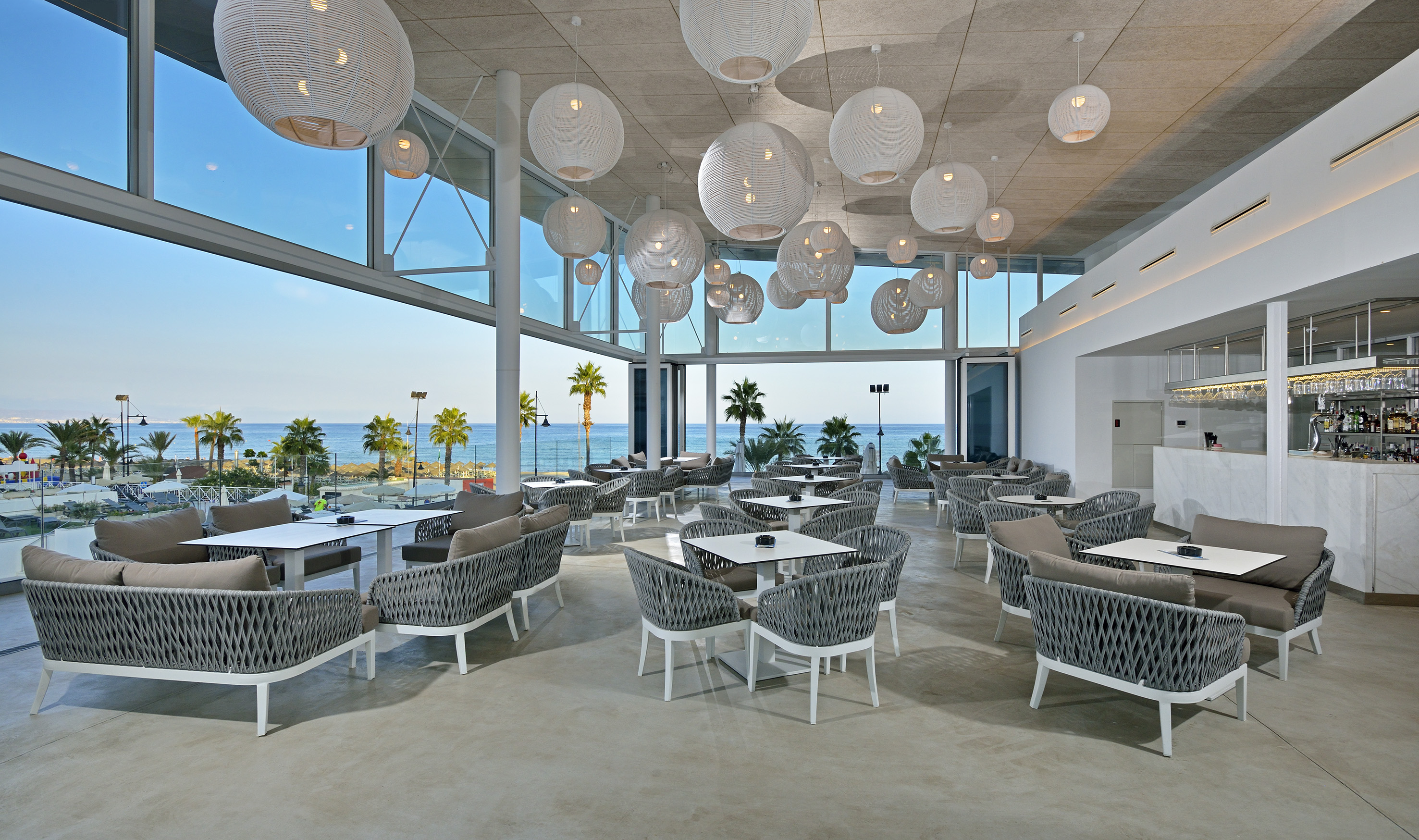 Modern beachside restaurant with ocean view, grey seating, and white tables.