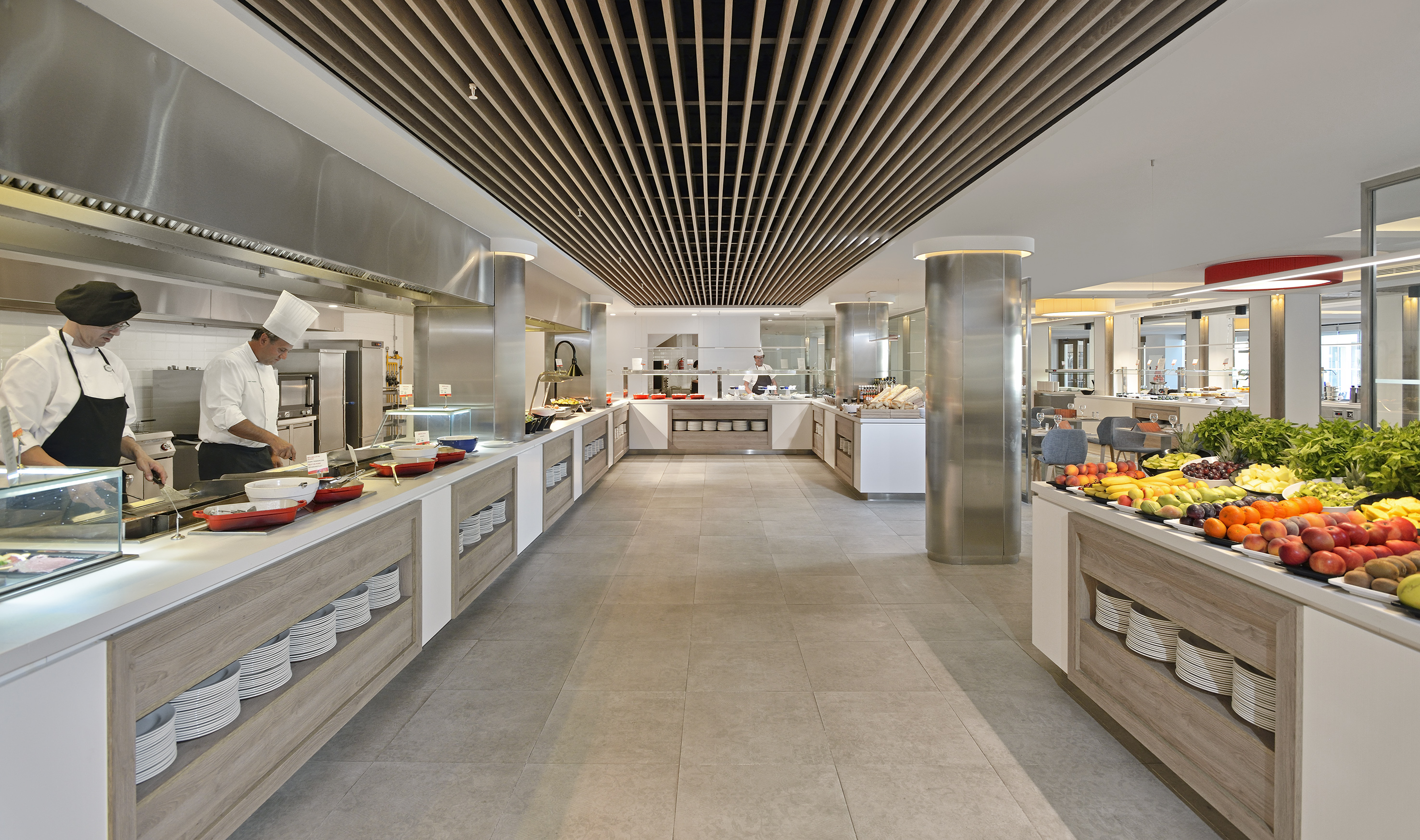 Modern buffet restaurant with chefs cooking, fresh fruit, and food counters.