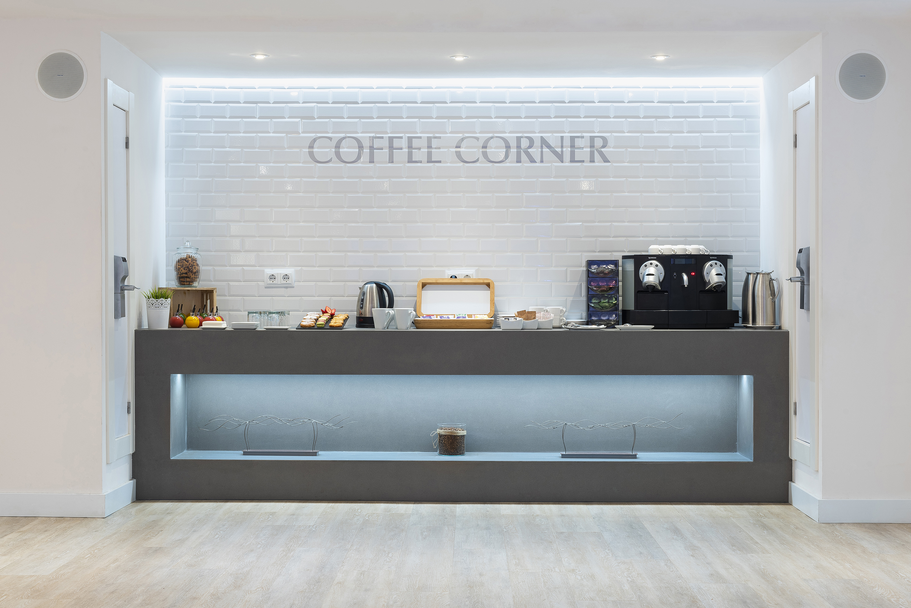 Modern self-service coffee corner with espresso machine, tea, and snacks.