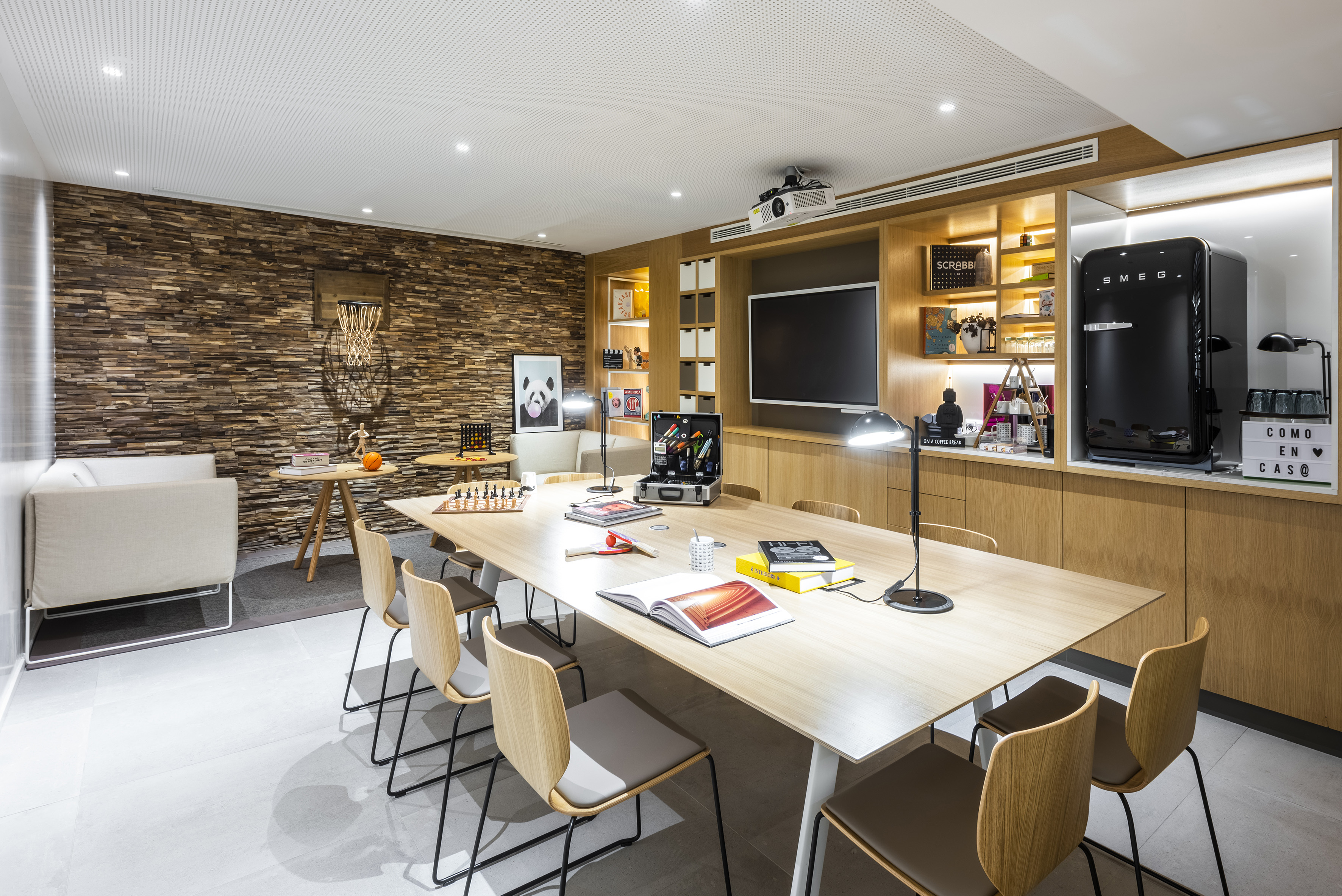 Modern multi-purpose room with wooden table, TV, projector, Smeg fridge.
