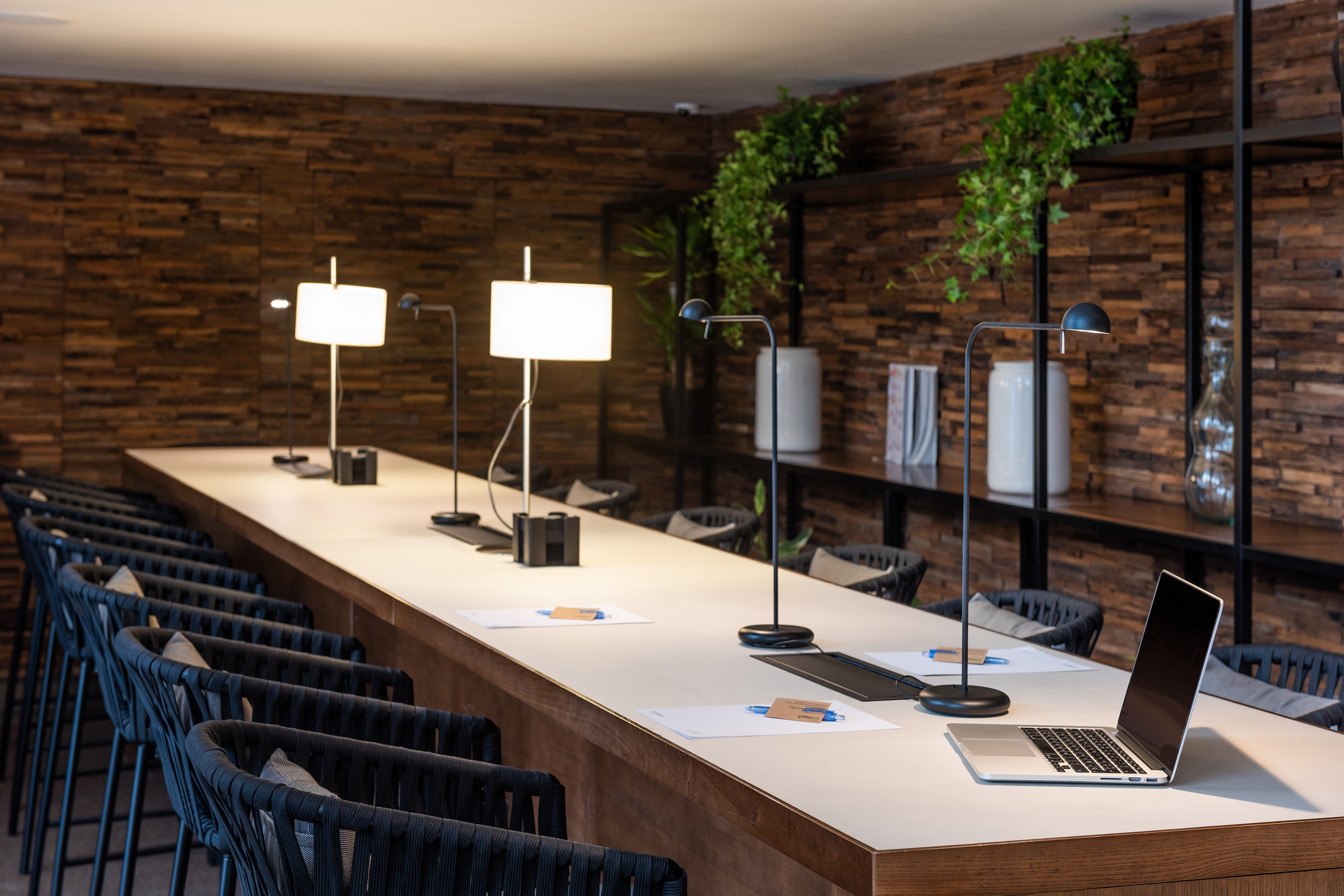 Modern co-working space with long desk, sleek lamps, and textured wood wall.