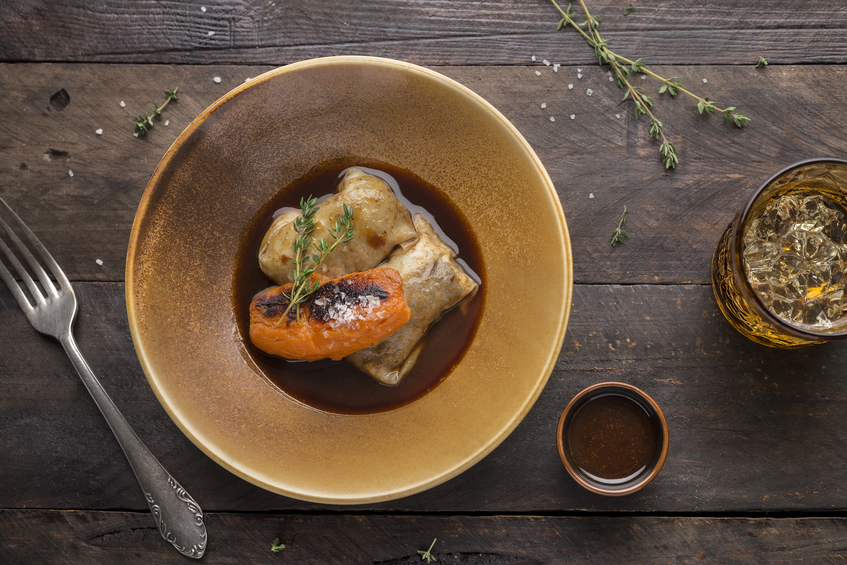 Plated cabbage rolls with grilled carrot, rich sauce, and thyme.