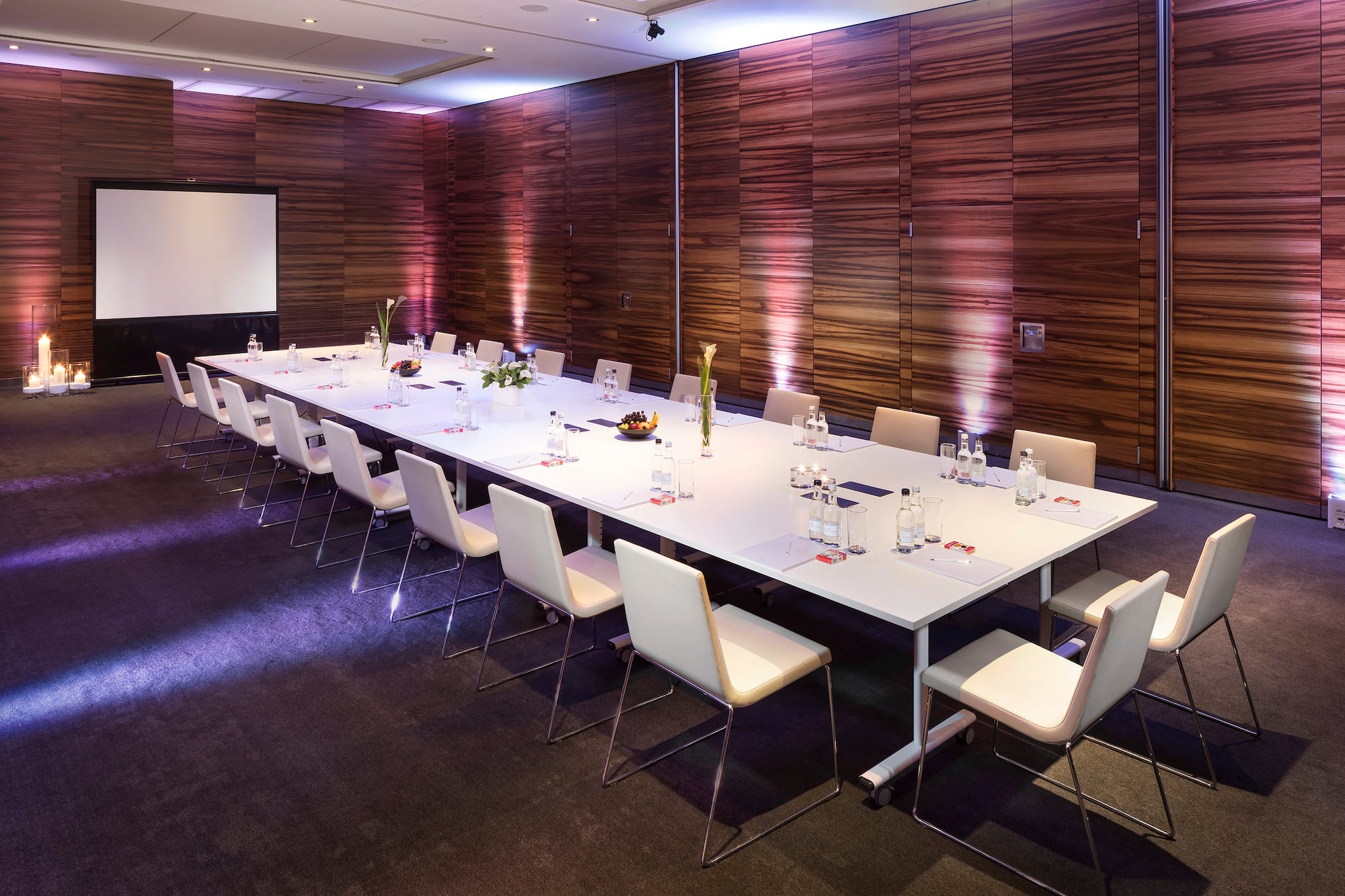 a long conference table with chairs and a projector screen