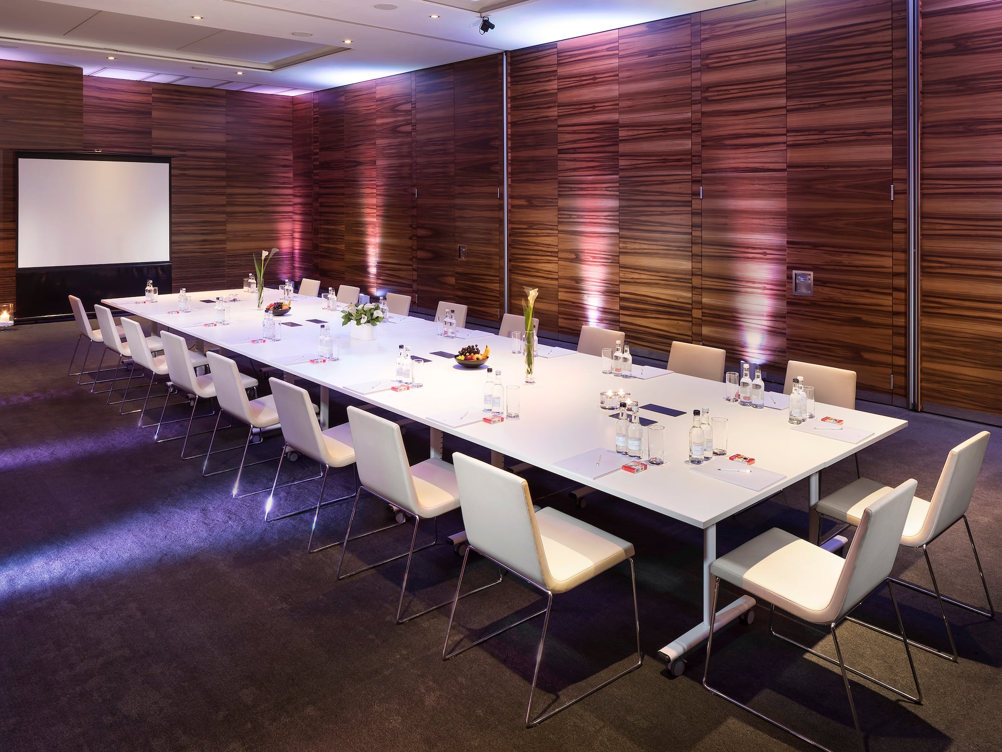 a long conference table with chairs and a projector screen