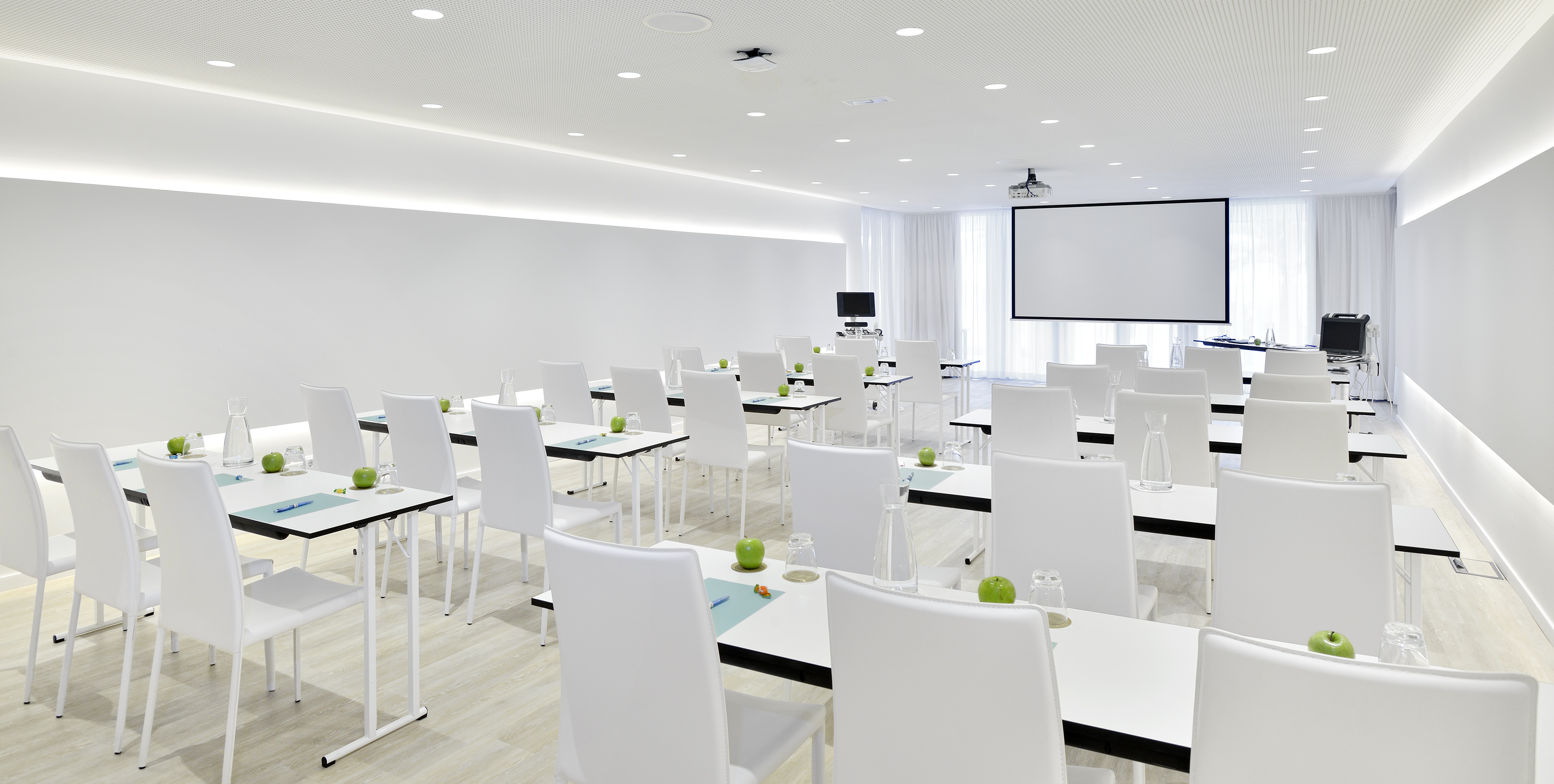 Bright white meeting room, projector screen, tables with green apples.