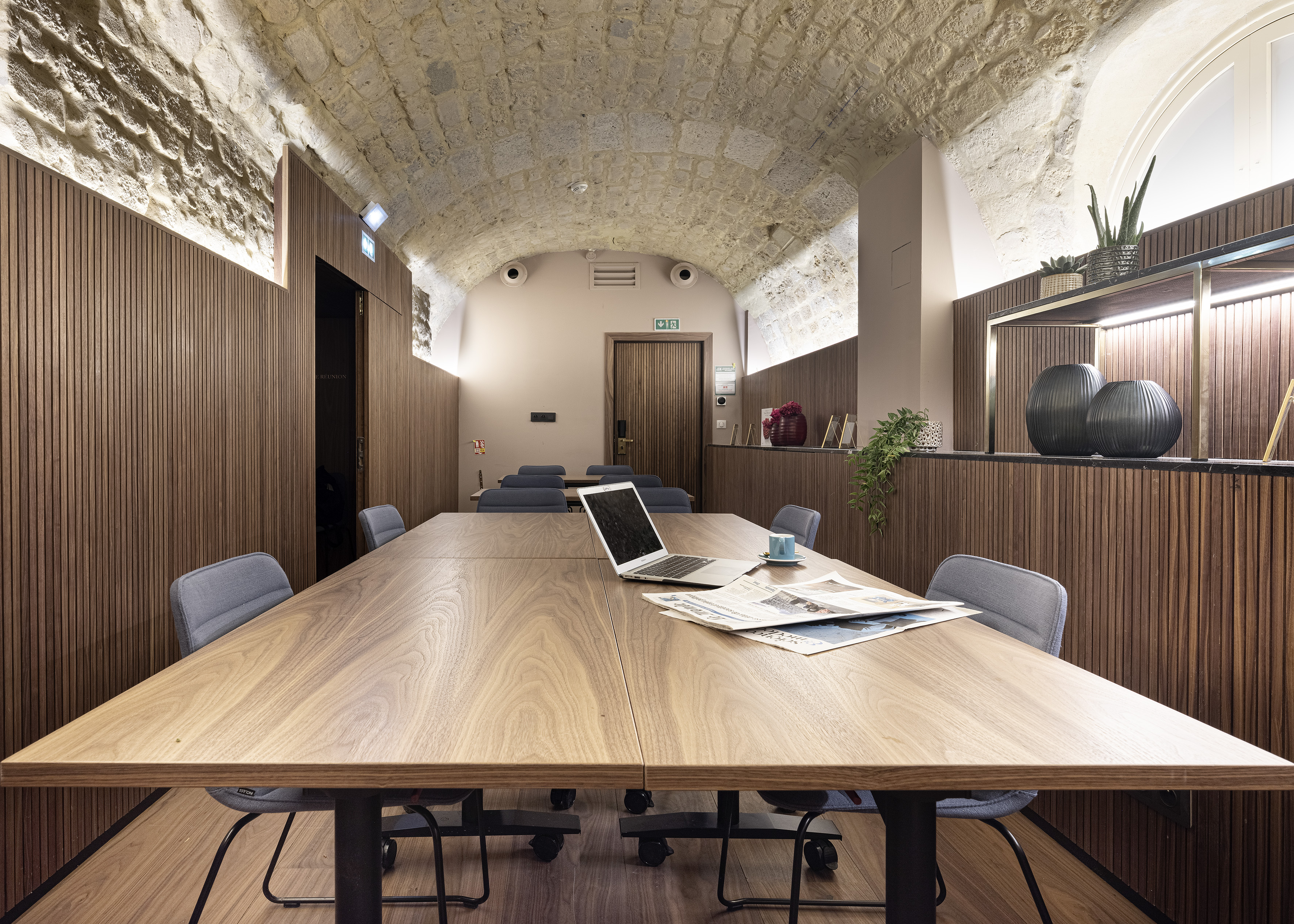 Modern conference room with large wood table, laptop, and vaulted stone ceiling.